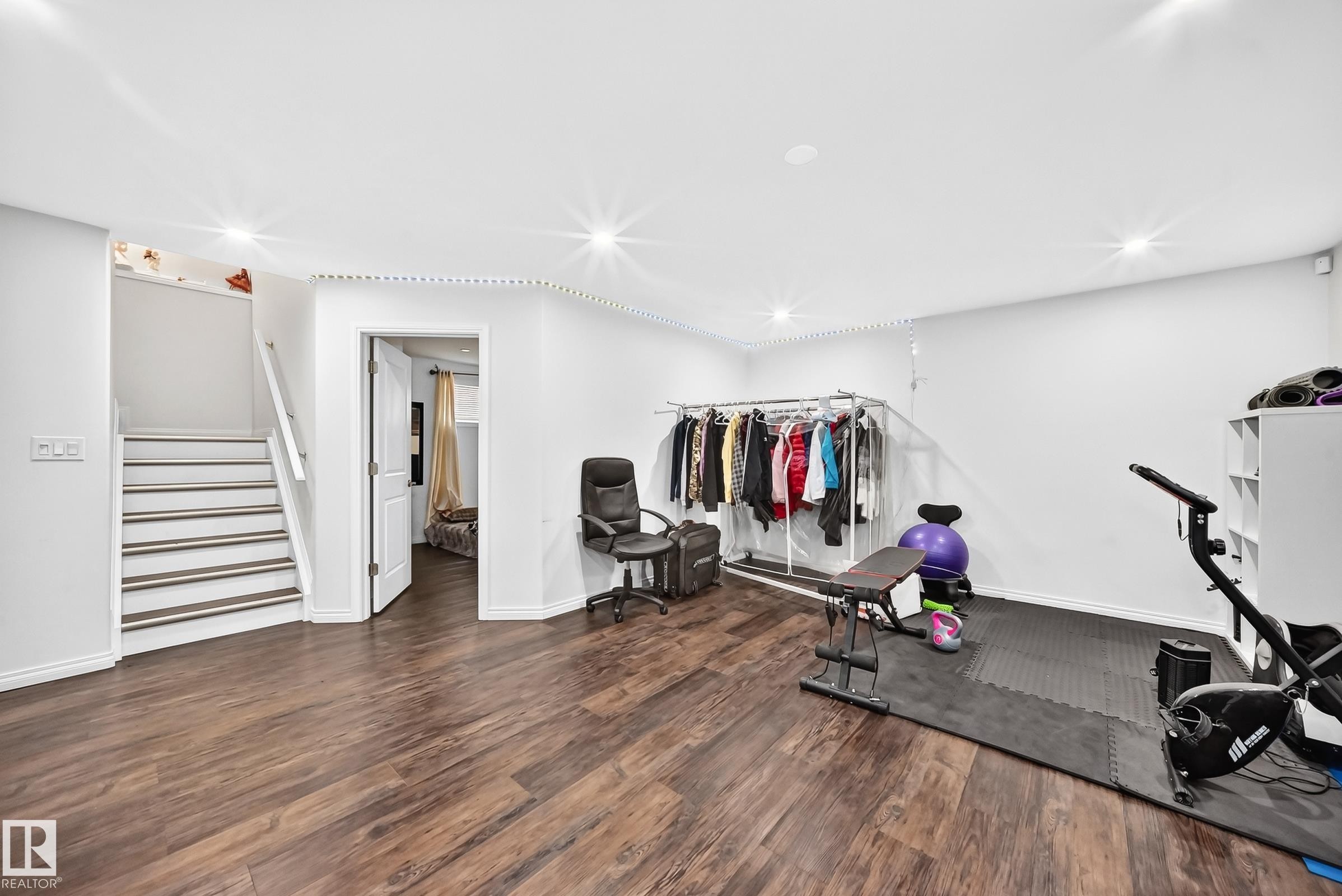 Spacious room featuring wood-finish flooring, recessed lighting, white walls, and a staircase with white risers and wood-finish treads - 12410 171A Avenue, Edmonton, AB