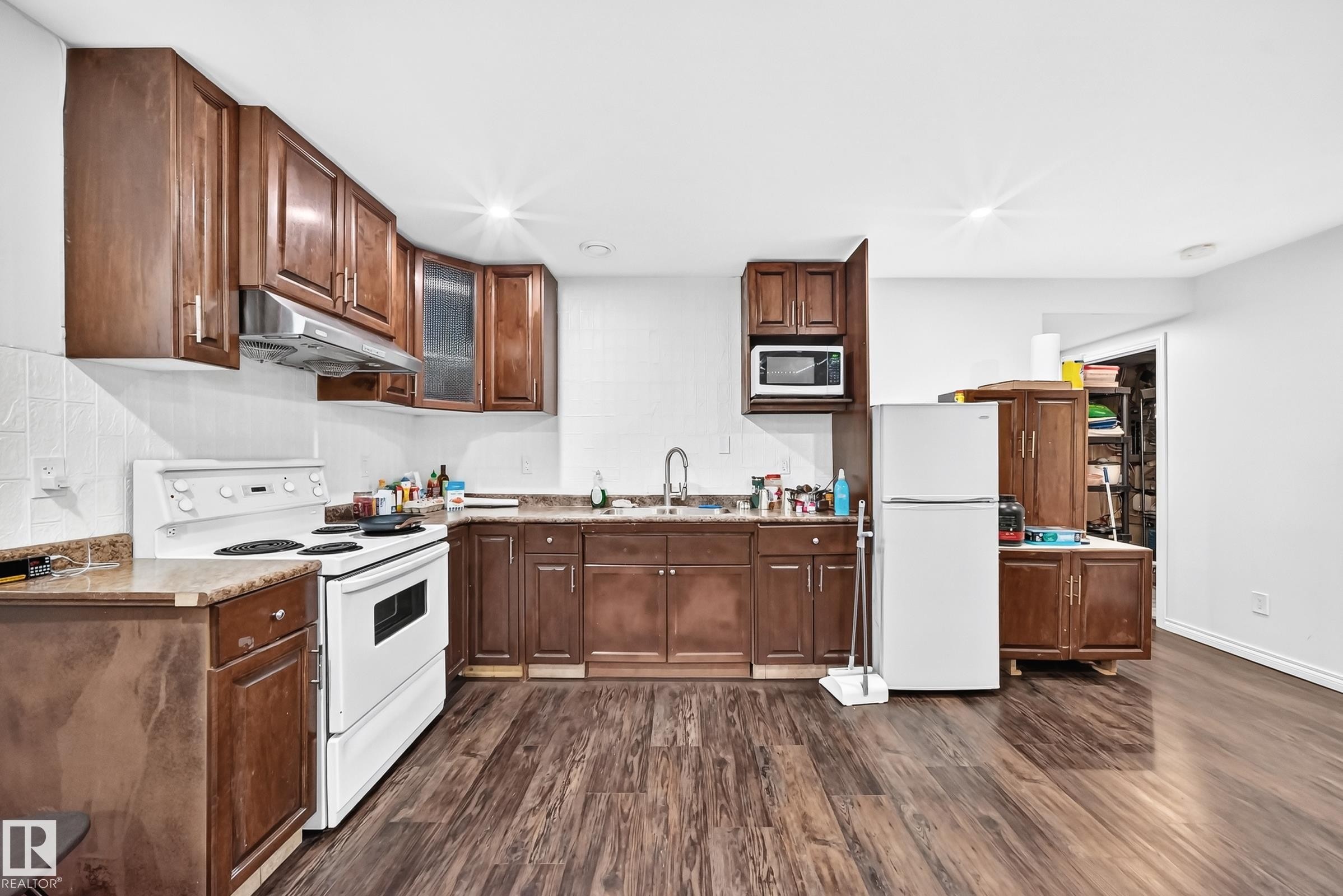 Kitchen featuring wood-finish flooring, white appliances, dark wood cabinetry, and laminate countertops - 12410 171A Avenue, Edmonton, AB