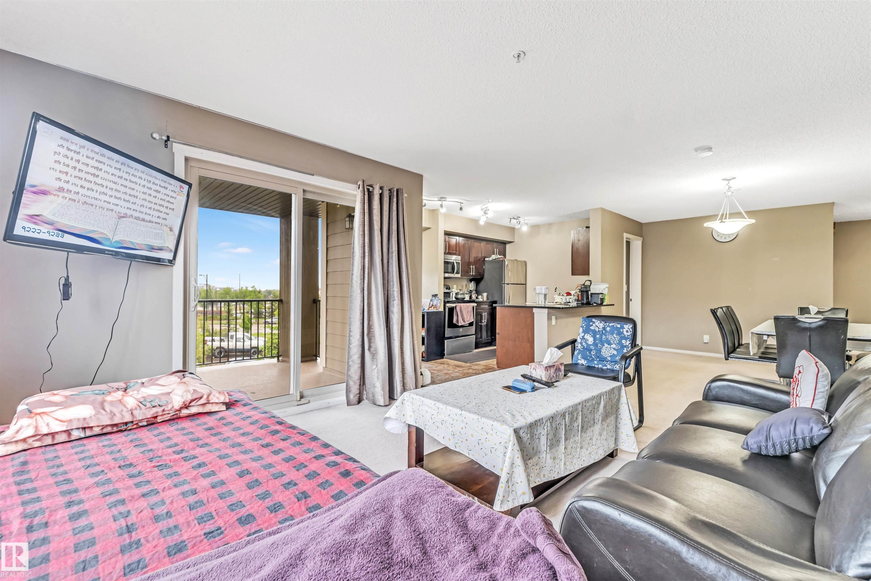 Open-concept living area featuring a kitchen with dark wood-finish cabinetry, a dining space with a contemporary chandelier, and a living room with light-colored carpeting - 225 111 Watt Common, Edmonton, AB