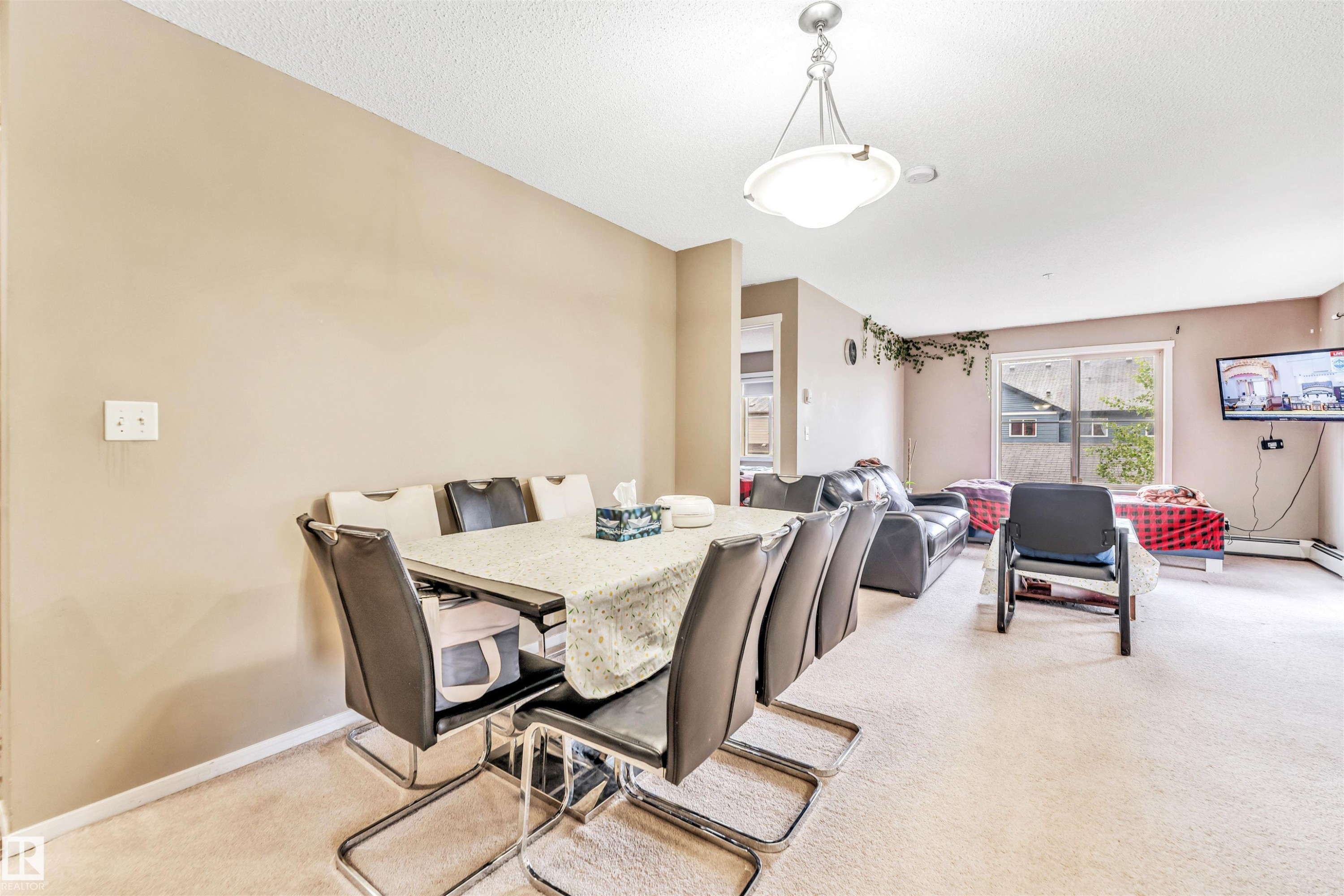Open-concept living area featuring neutral-toned walls, carpet flooring, a ceiling-mounted light fixture, and a sliding glass door - 225 111 Watt Common, Edmonton, AB