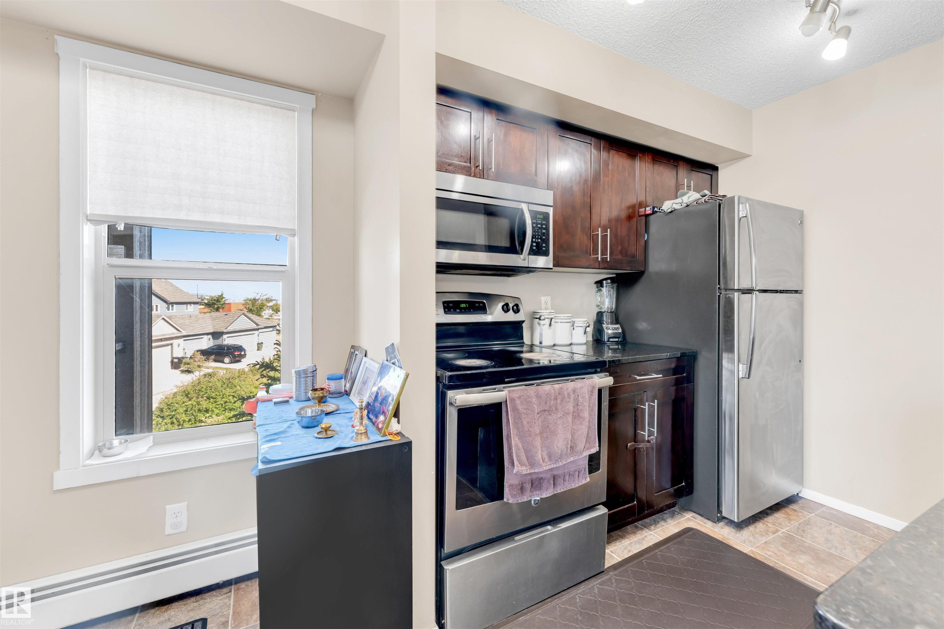 Kitchen featuring stainless steel appliances, dark wood cabinetry, black countertops, and wood-finish flooring - 225 111 Watt Common, Edmonton, AB