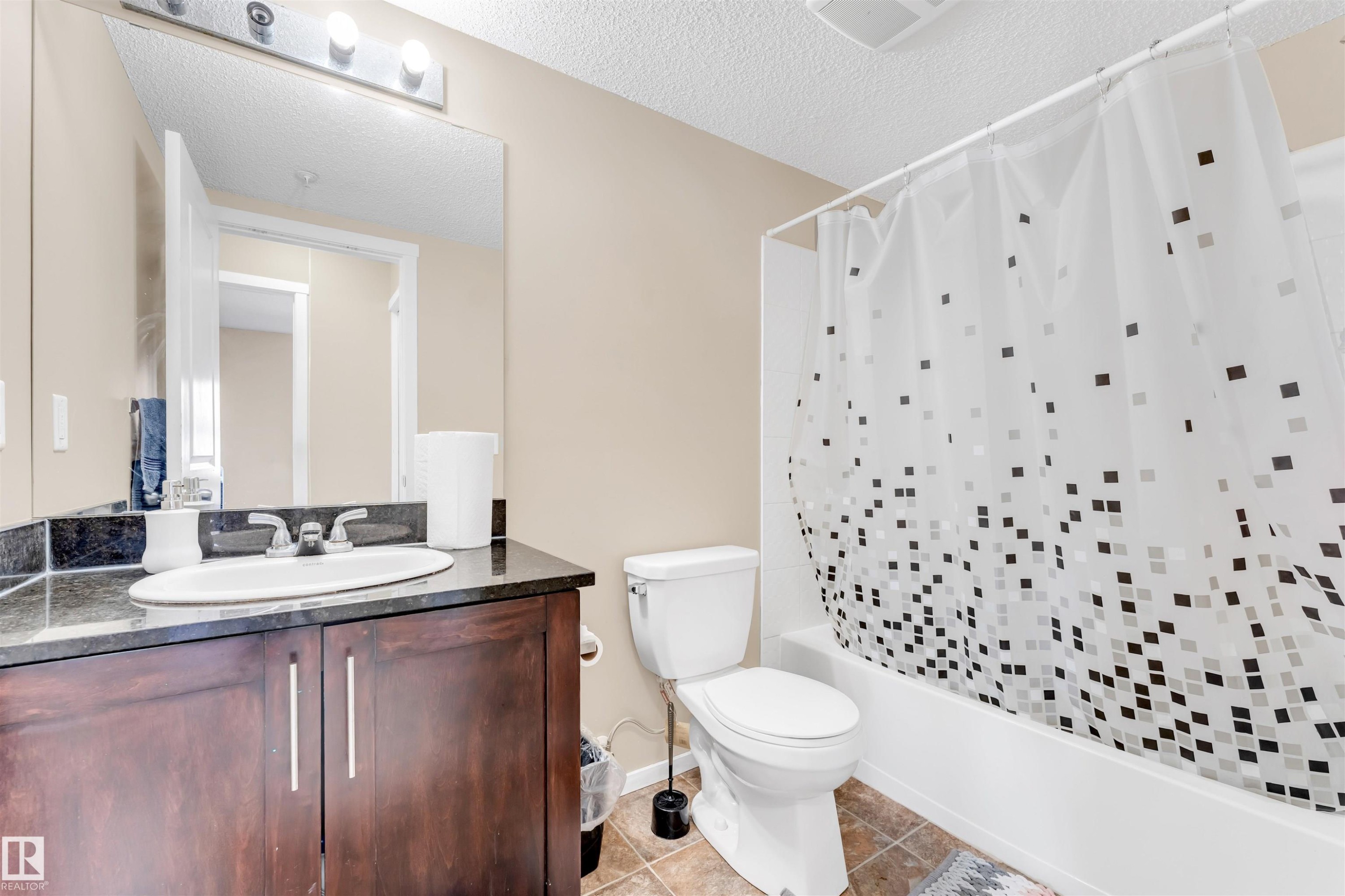 Bathroom featuring a dark wood-finish vanity with an undermount sink, a dark stone-finish countertop, and a large wall-mounted mirror - 225 111 Watt Common, Edmonton, AB
