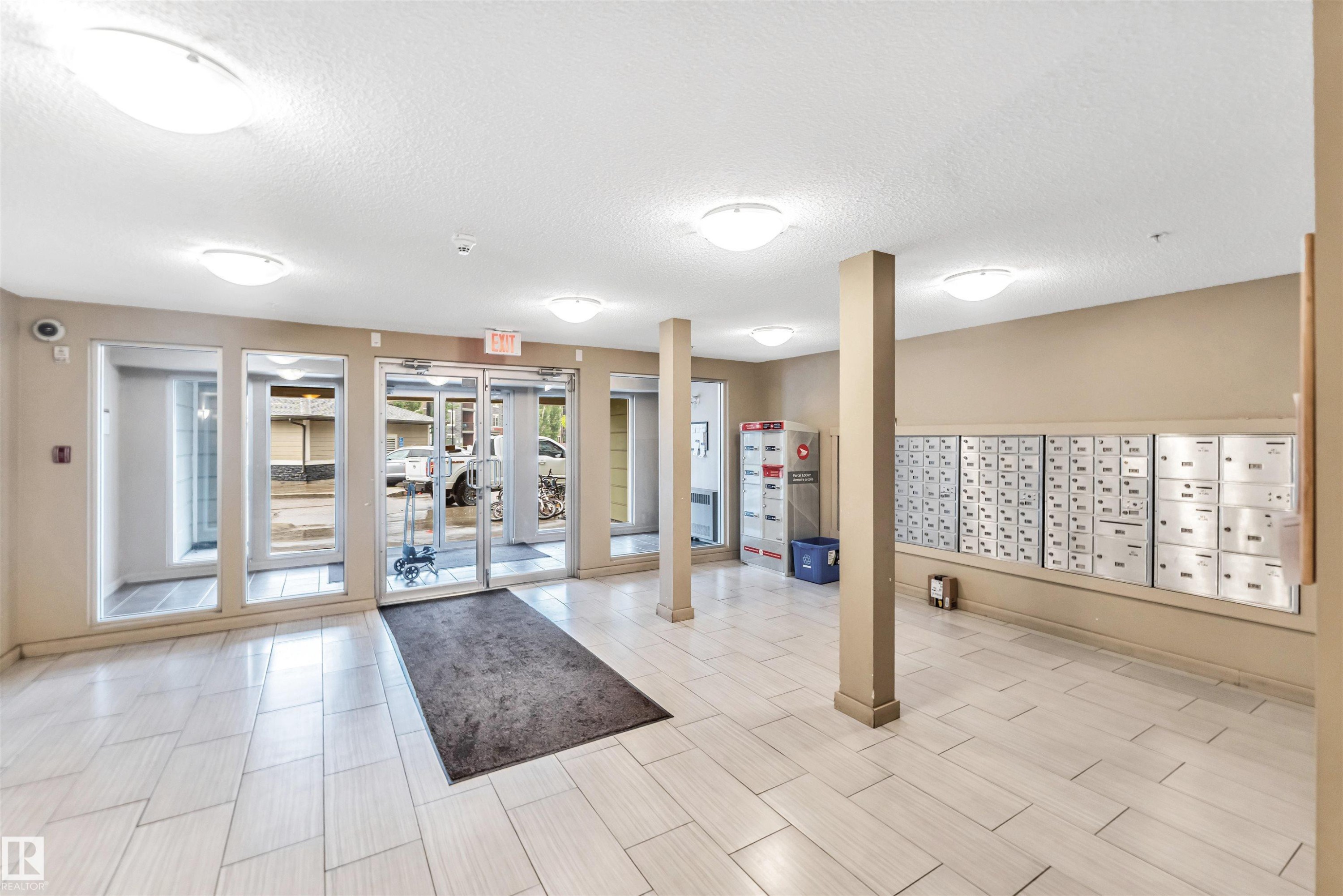 Spacious communal entry foyer featuring light-toned tile flooring, recessed lighting, and a wall of individual mailboxes - 225 111 Watt Common, Edmonton, AB