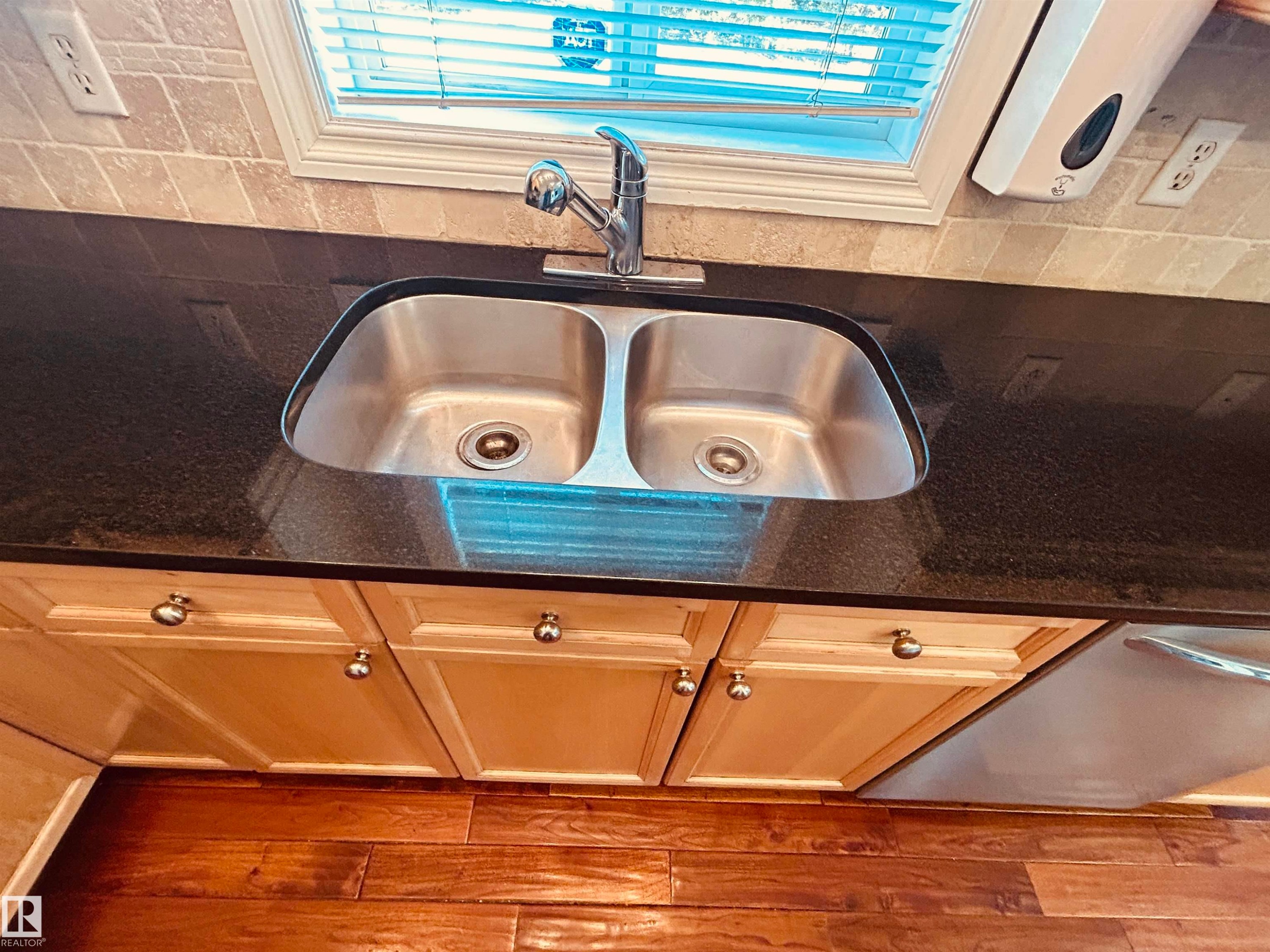 Under-mount stainless steel double basin sink with a chrome faucet set into a dark countertop, complemented by a tiled backsplash - 89 12050 17 Avenue, Edmonton, AB
