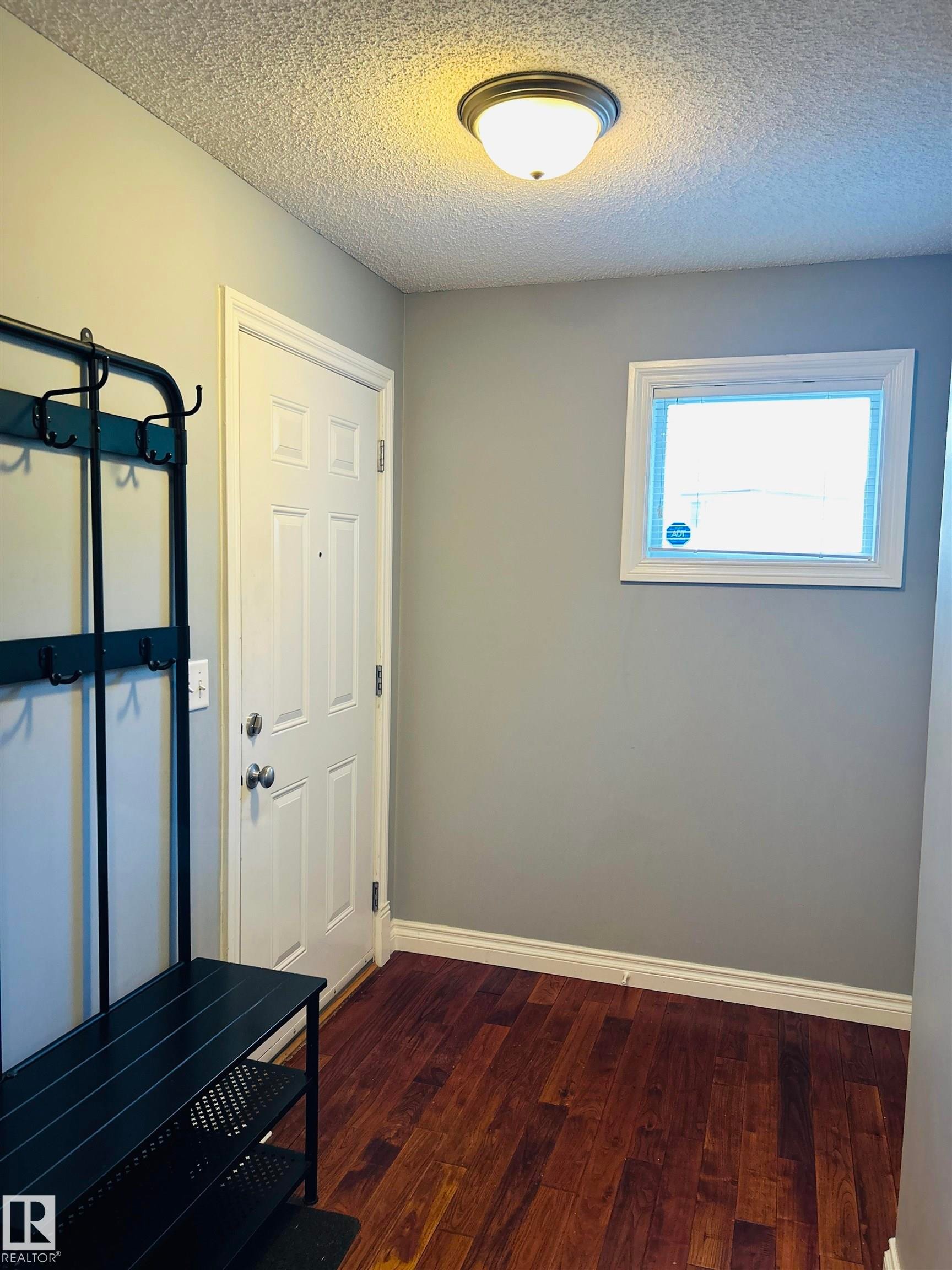 Inviting entryway featuring wood-finish flooring, a paneled door, and a flush-mount ceiling light - 89 12050 17 Avenue, Edmonton, AB