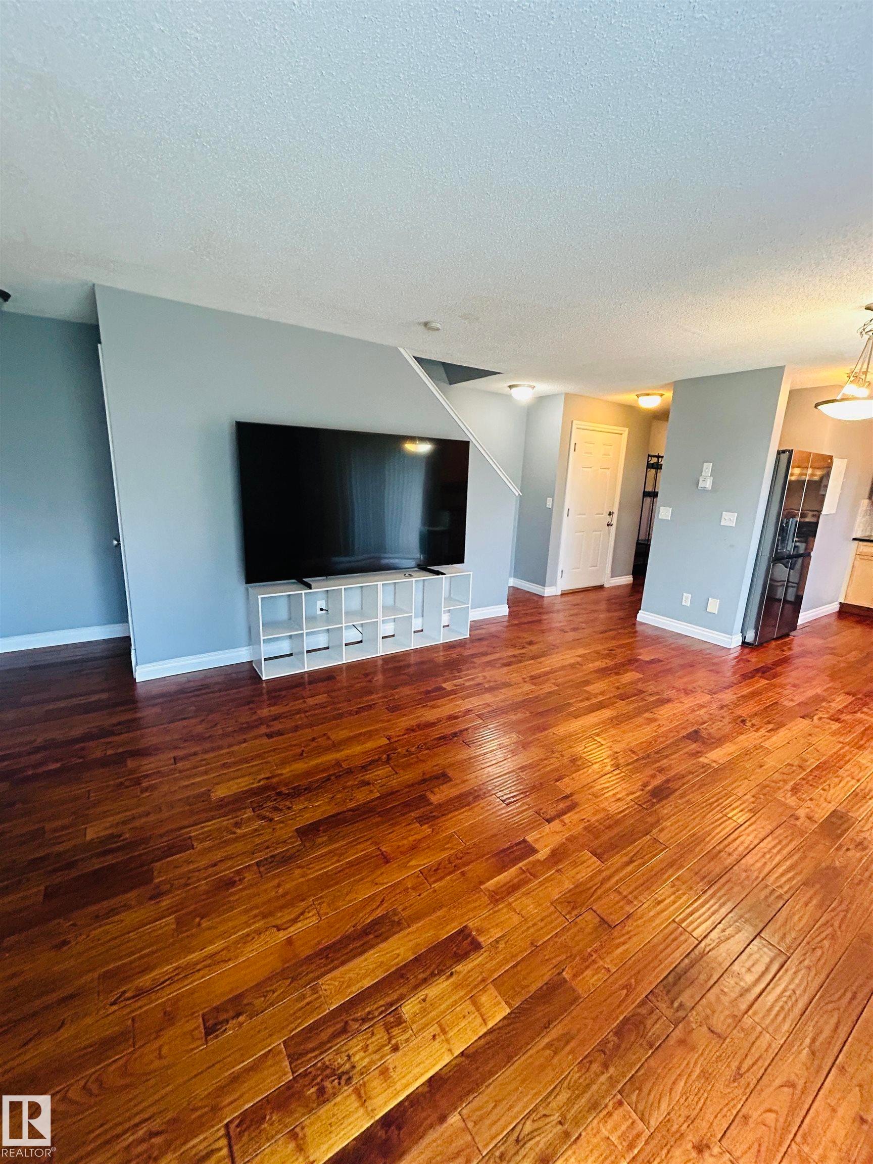 Rich wood-finish flooring extending through an open-concept living area - 89 12050 17 Avenue, Edmonton, AB