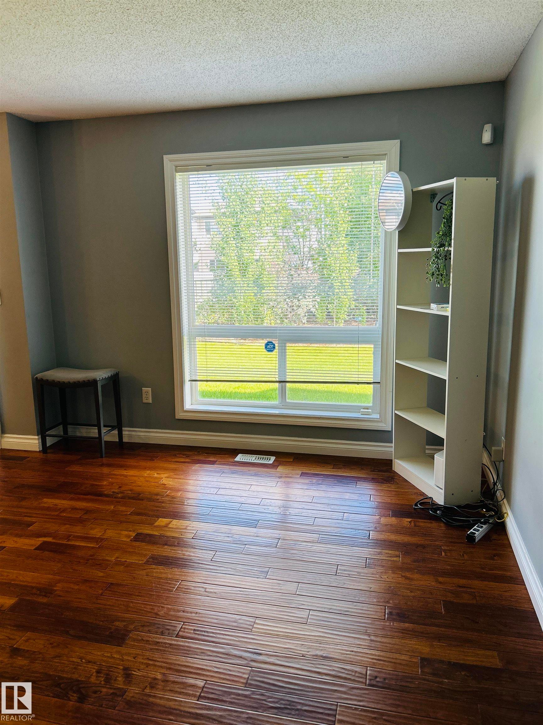 Hardwood-look flooring complemented by a large window with white trim, offering ample natural light, and neutral gray wall tones - 89 12050 17 Avenue, Edmonton, AB