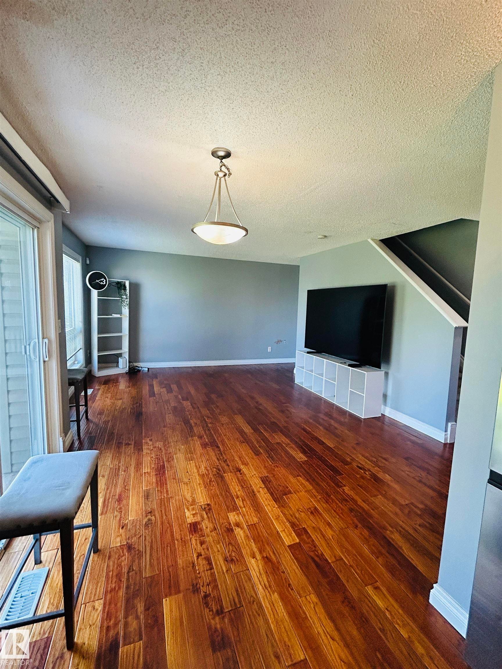 Spacious living area featuring rich wood-finish flooring, a modern semi-flush mount light fixture, neutral wall colors, and white trim - 89 12050 17 Avenue, Edmonton, AB