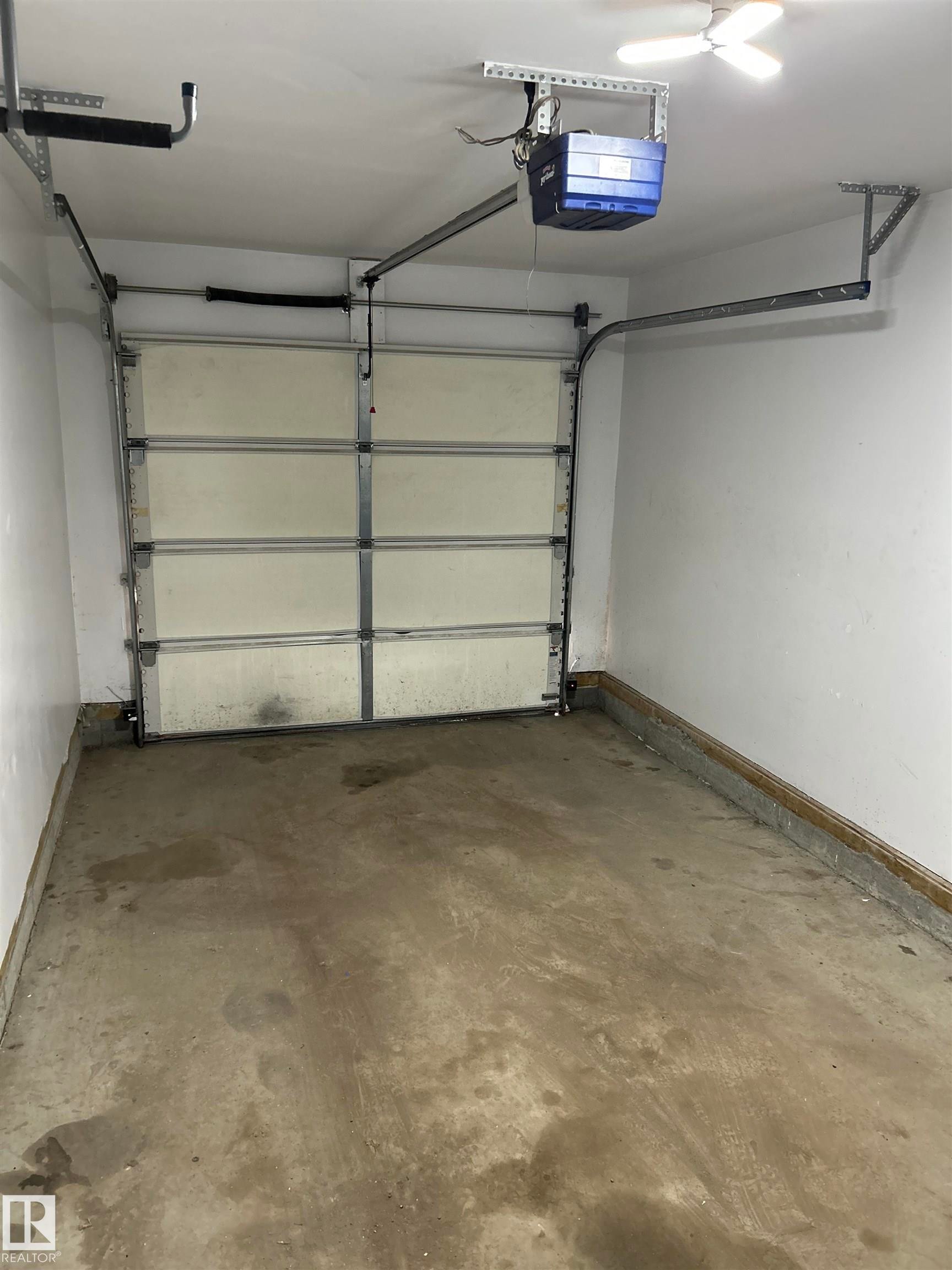 Single-car garage featuring a sectional overhead door with an automatic opener, concrete flooring, and overhead lighting - 89 12050 17 Avenue, Edmonton, AB