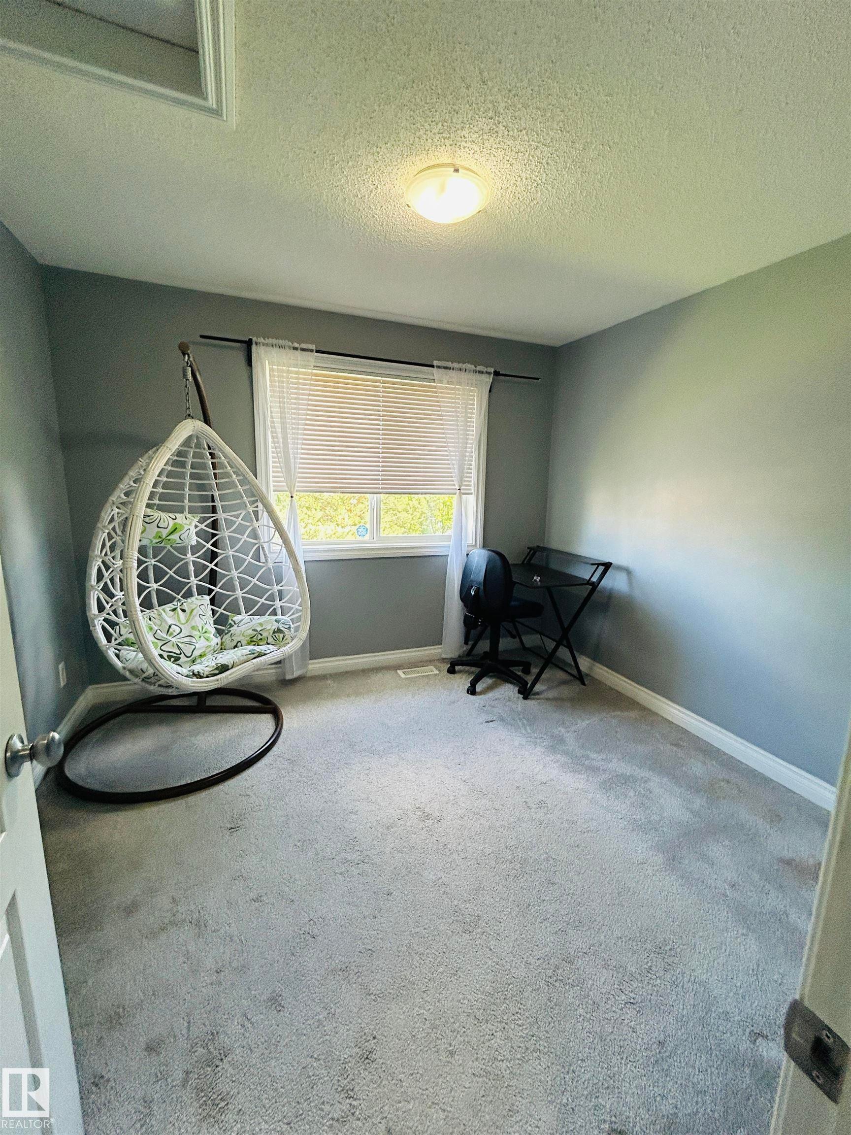 Carpeted room featuring a single window with blinds and a flush mount ceiling light fixture - 89 12050 17 Avenue, Edmonton, AB