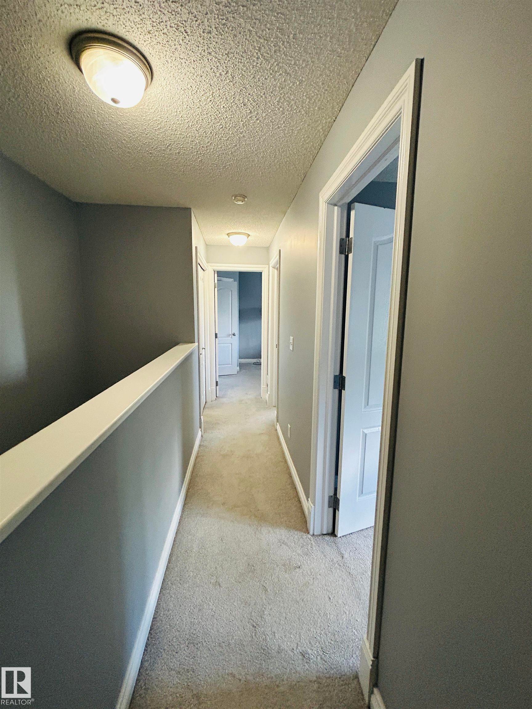 Hallway featuring neutral-toned carpet, light gray walls, and white trim - 89 12050 17 Avenue, Edmonton, AB