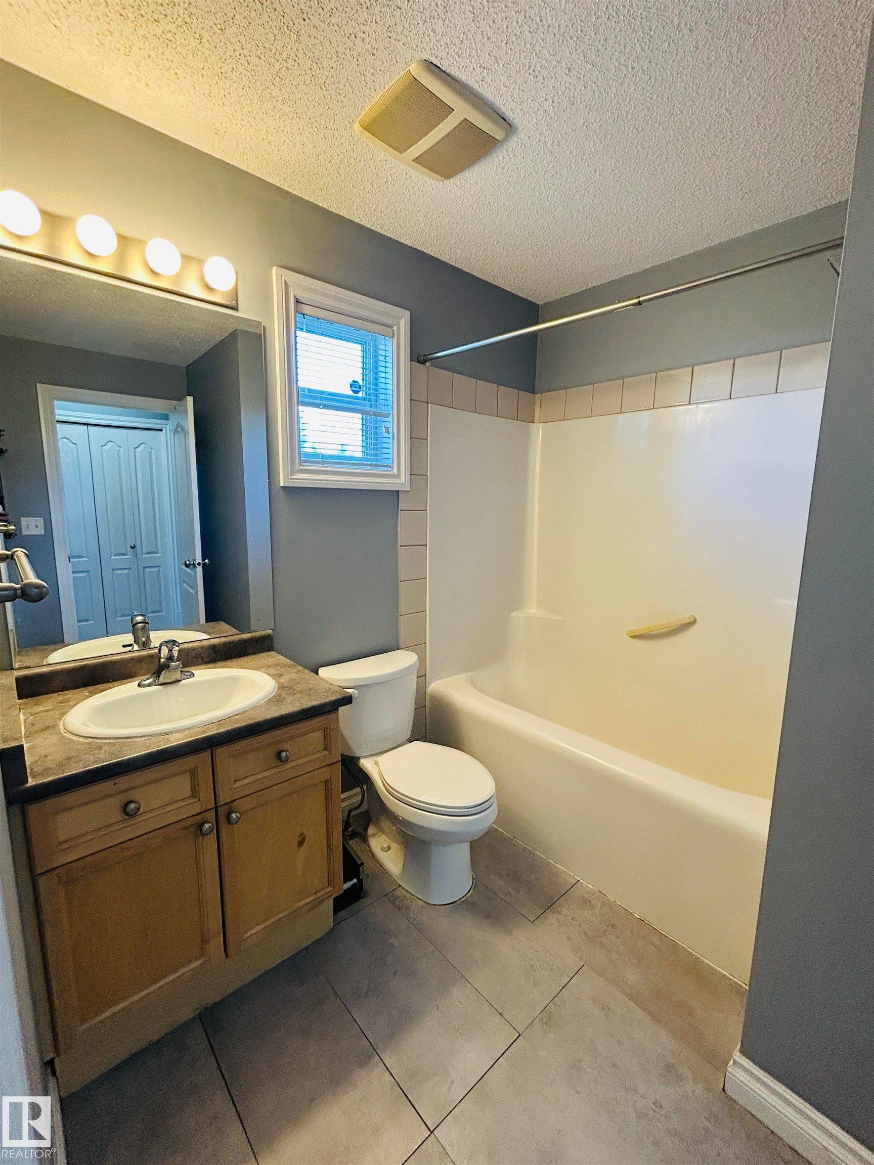 Full bathroom with a wood-finish vanity, integrated sink, and dark countertop - 89 12050 17 Avenue, Edmonton, AB