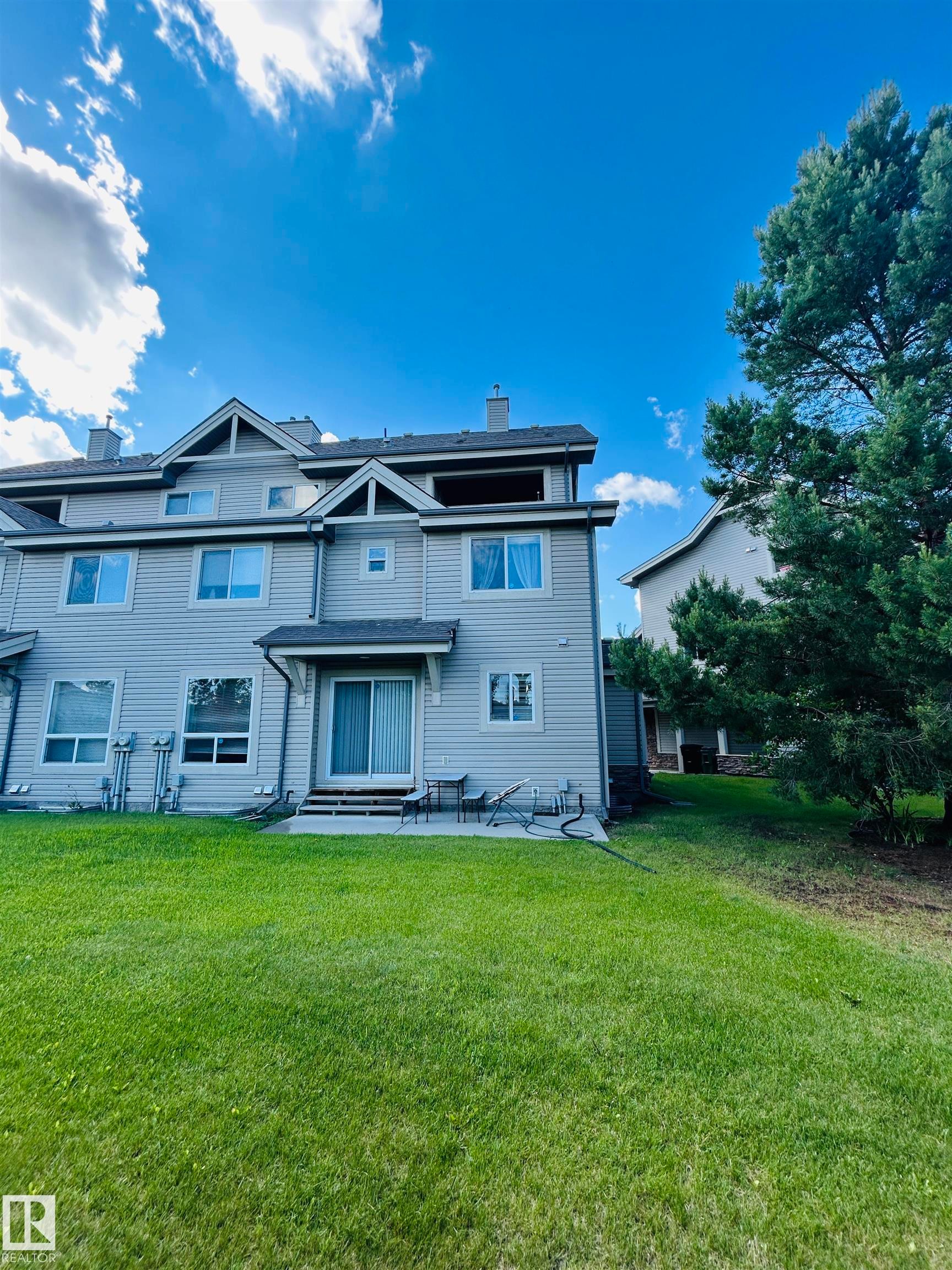 Rear exterior with siding, featuring multiple windows, a sliding glass door, a patio area, and a substantial lawn - 89 12050 17 Avenue, Edmonton, AB