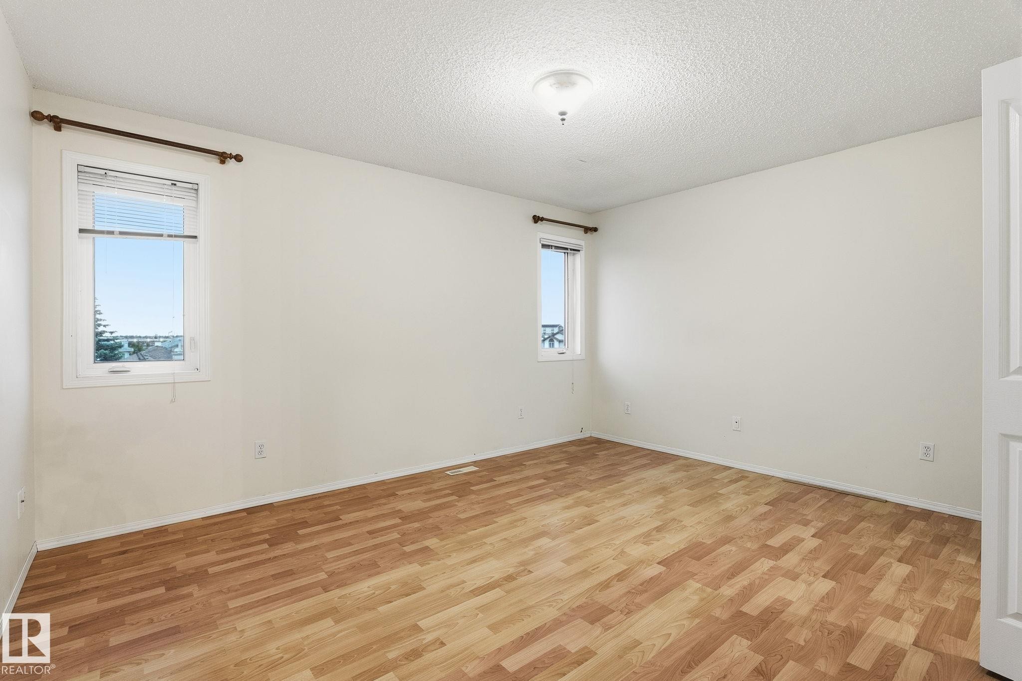 Spacious room featuring wood-finish flooring, white walls, and a textured ceiling - 1906 37B Av Nw, Edmonton, AB - Indoor Photo Showing Other Room