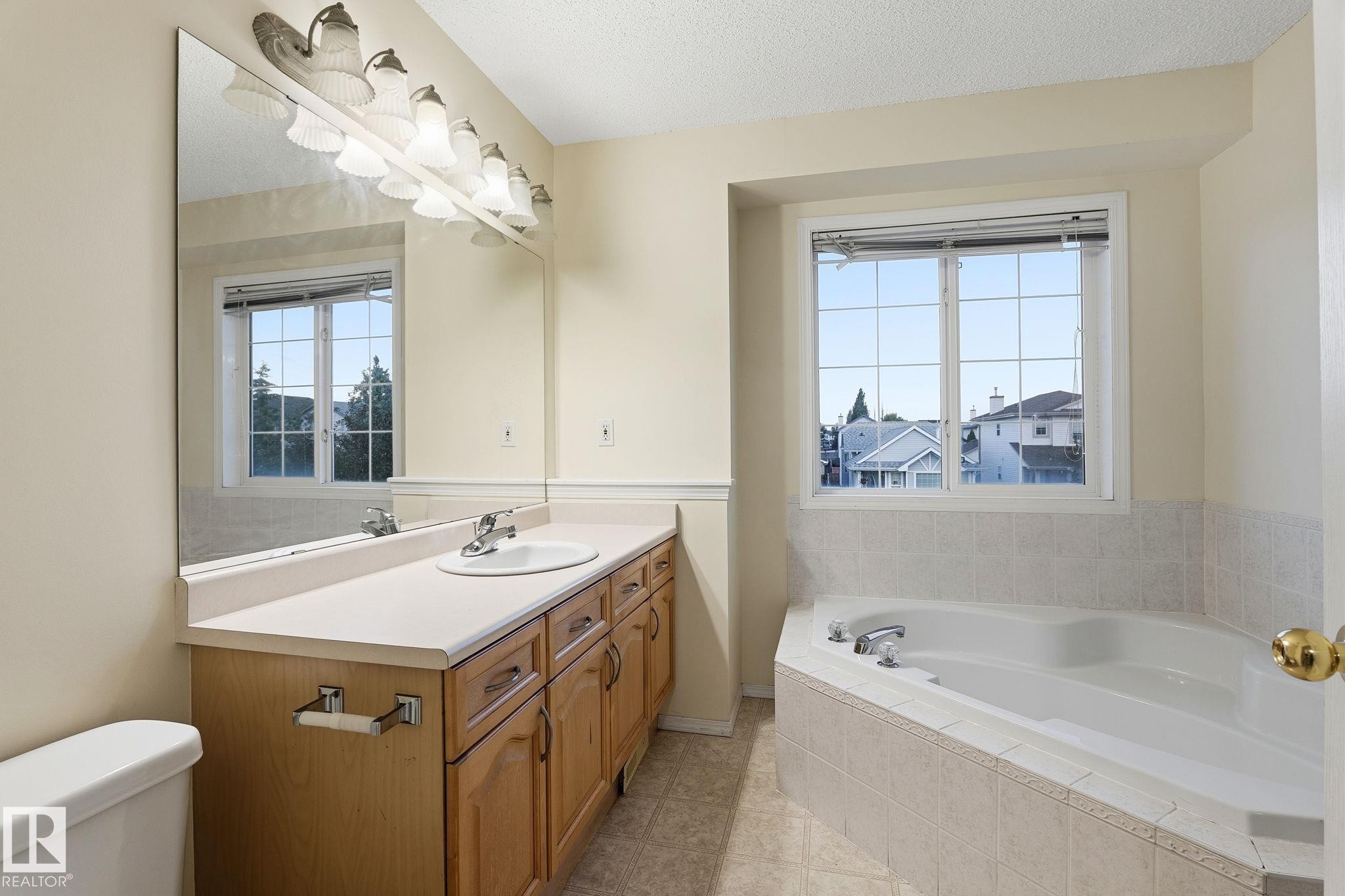 Spacious bathroom featuring a corner soaking tub, a long vanity with dual sinks, and a large mirror with integrated lighting - 1906 37B Av Nw, Edmonton, AB - Indoor Photo Showing Bathroom