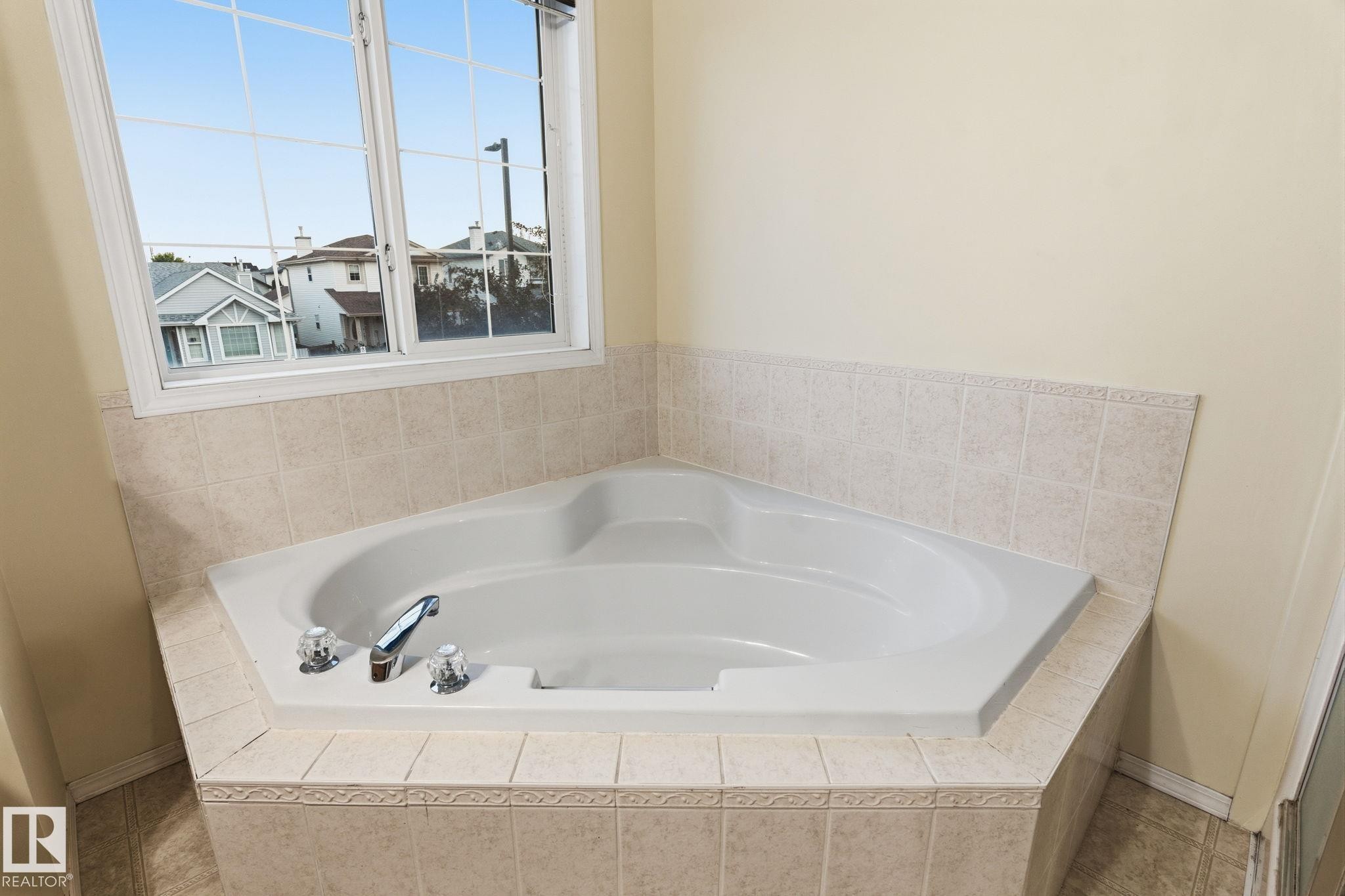 Corner soaking tub with tiled surround and window above - 1906 37B Av Nw, Edmonton, AB - Indoor Photo Showing Bathroom