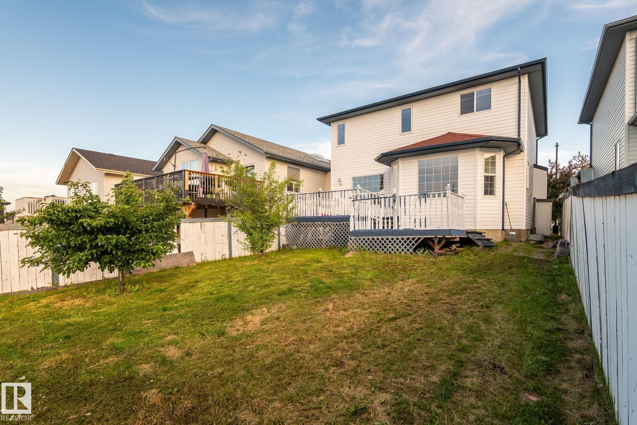 Expansive backyard featuring a partial white fence, mature greenery, and sloped lawn - 1906 37B Av Nw, Edmonton, AB - Outdoor With Deck Patio Veranda