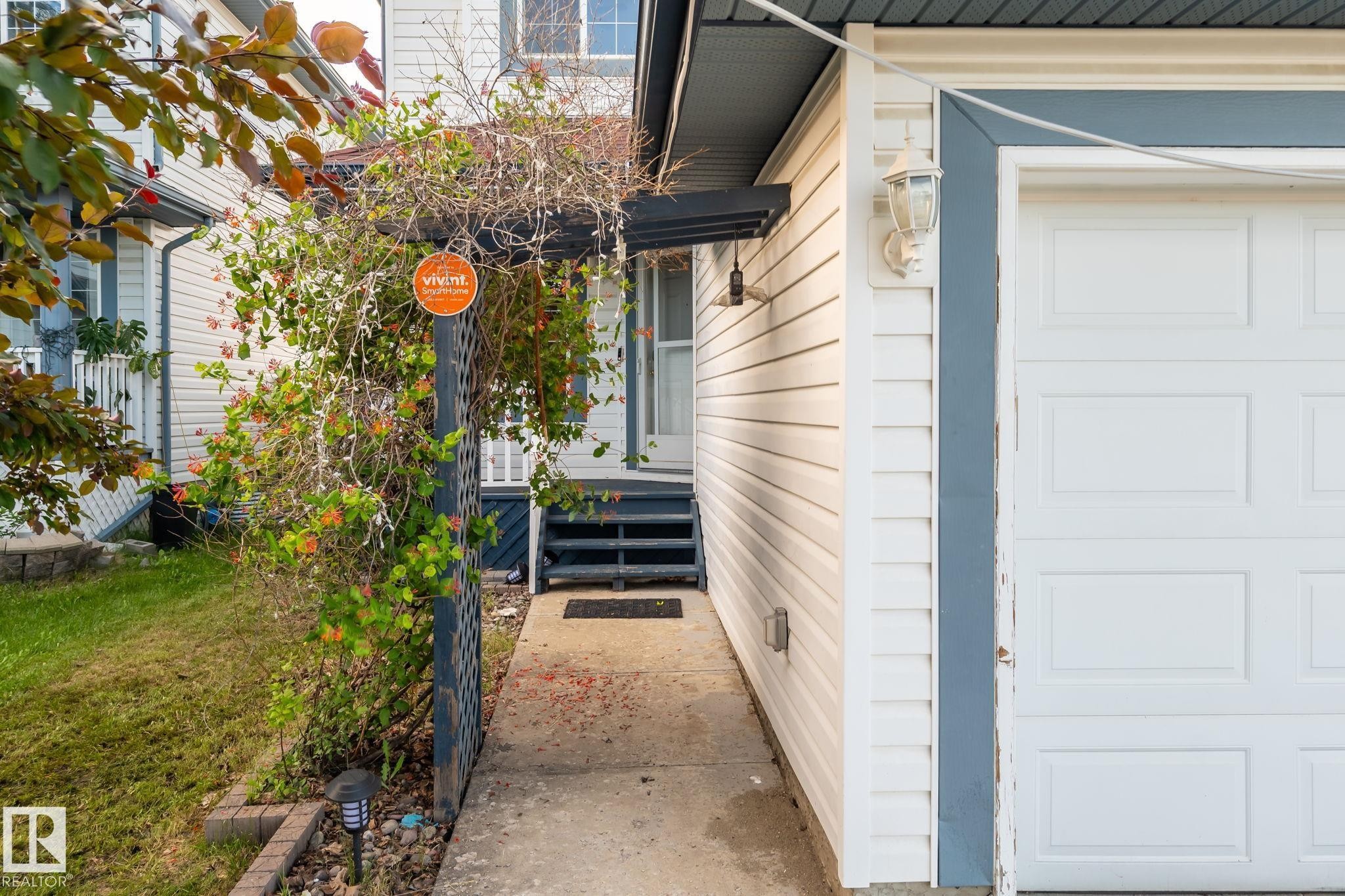 White siding exterior with a paneled garage door and a decorative wall lantern - 1906 37B Av Nw, Edmonton, AB - Outdoor With Exterior