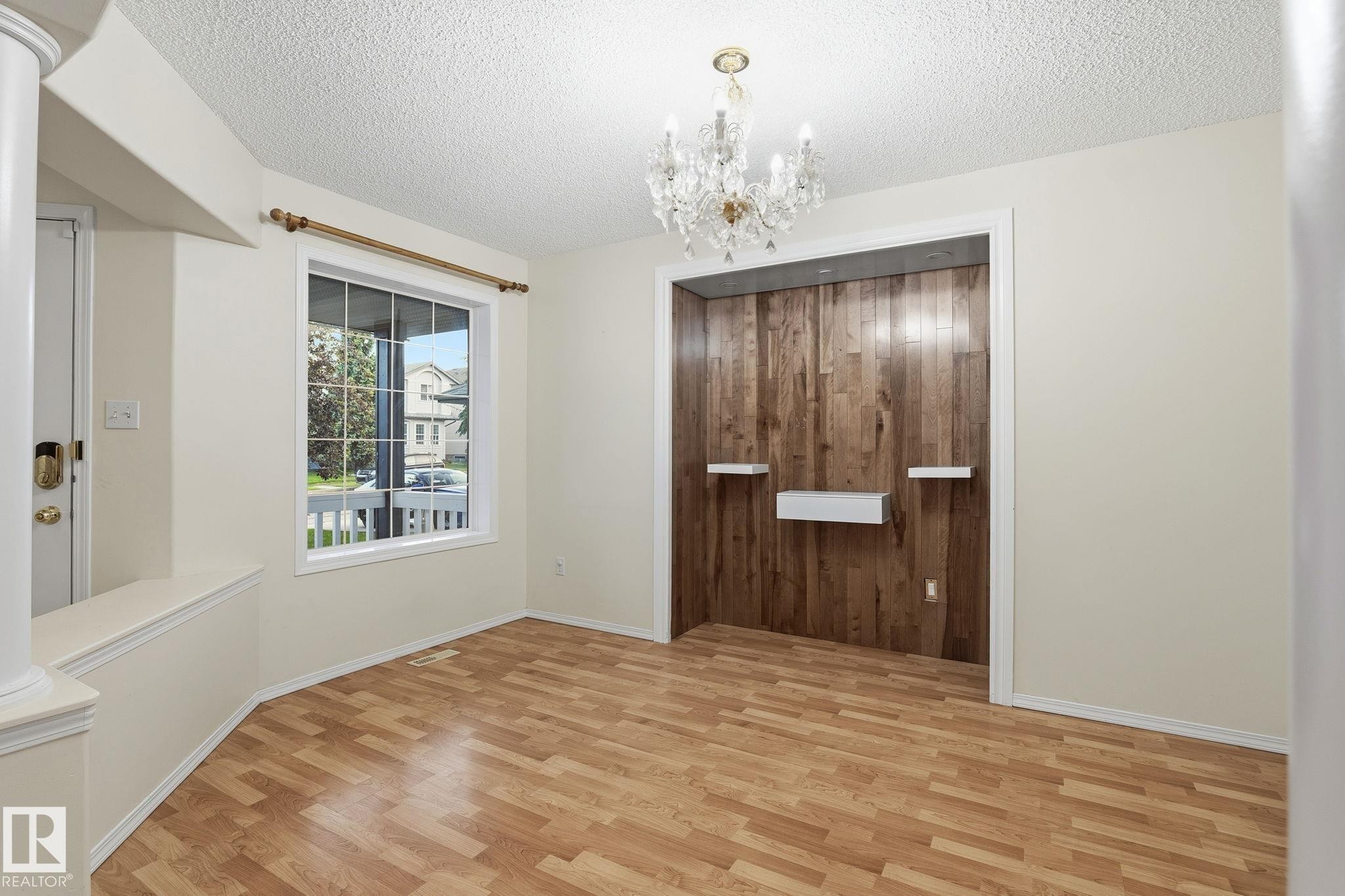 Interior space featuring wood-finish flooring, a crystal chandelier, and a recessed wall with vertical wood paneling - 1906 37B Av Nw, Edmonton, AB - Indoor Photo Showing Other Room
