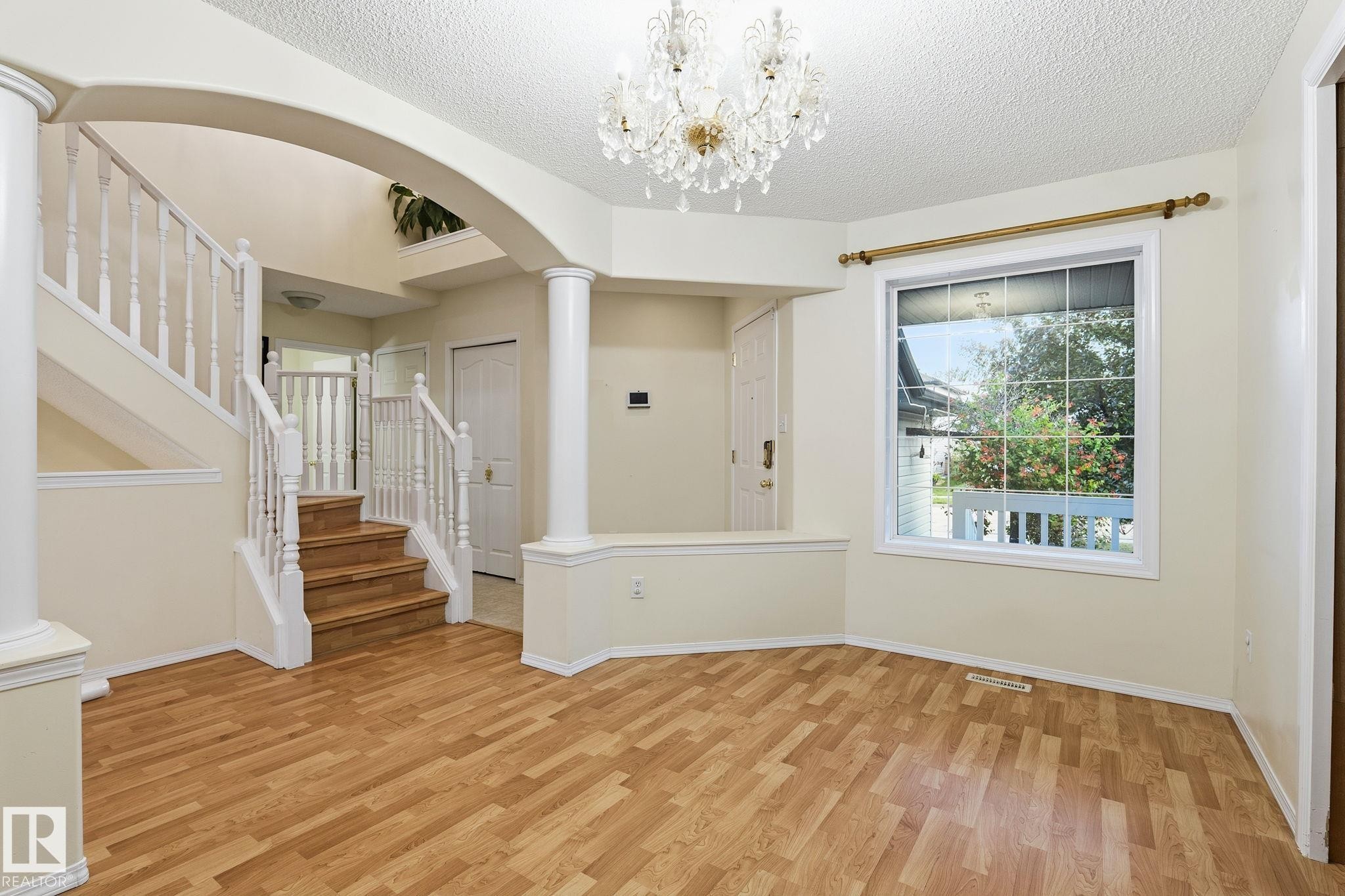 Open-concept space featuring wood-finish flooring, a grand staircase with white balusters, and an arched entry - 1906 37B Av Nw, Edmonton, AB - Indoor Photo Showing Other Room