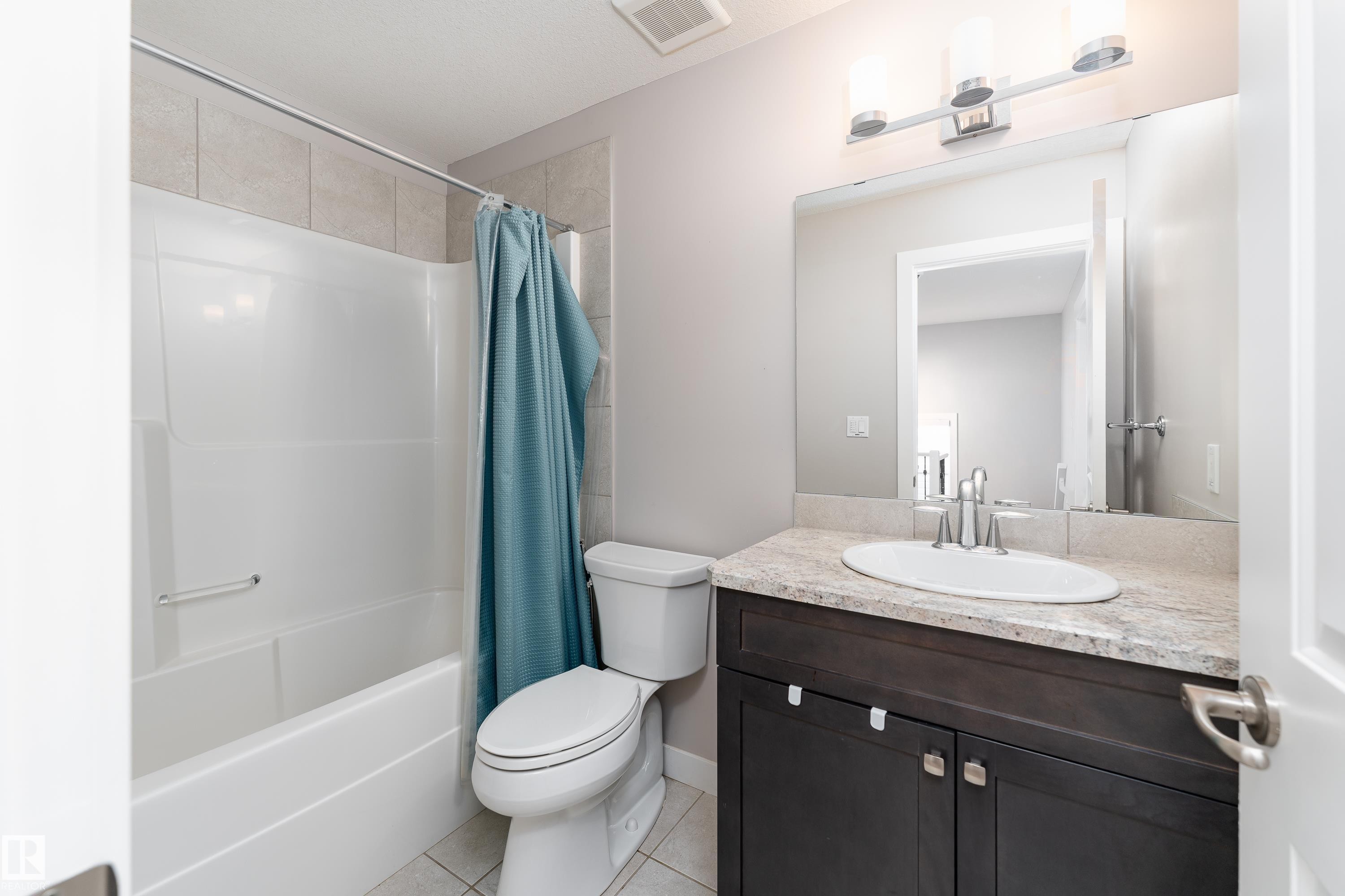 Bathroom featuring a white bathtub/shower combination with tile surround, a dark wood-finish vanity with a light-toned countertop, an oval undermount sink, and chrome fixtures - 191 Reed Place, Leduc, AB - Indoor Photo Showing Bathroom