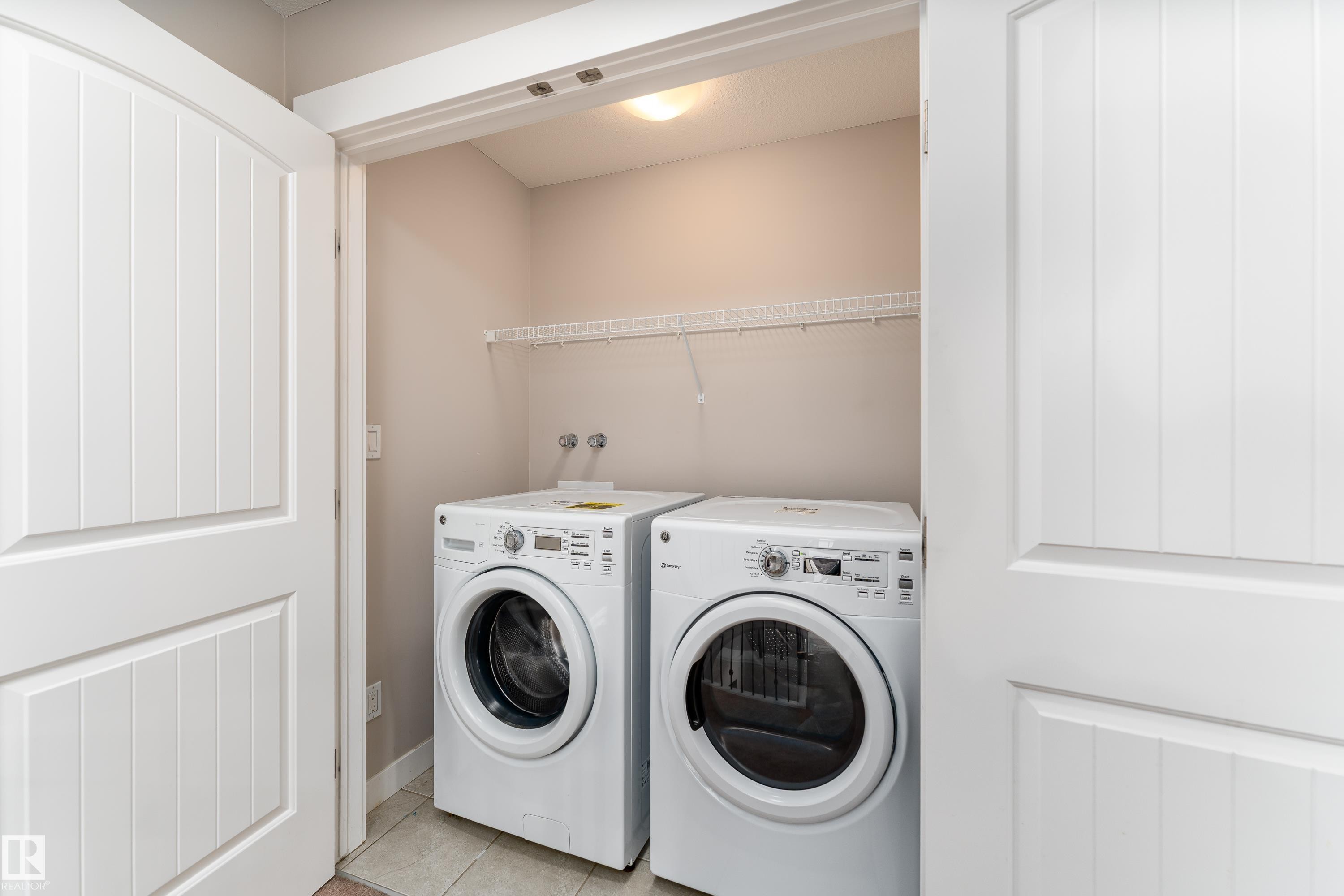 Laundry closet featuring a front-loading washer and dryer, tile flooring, and a wire shelving unit - 191 Reed Place, Leduc, AB - Indoor Photo Showing Laundry Room