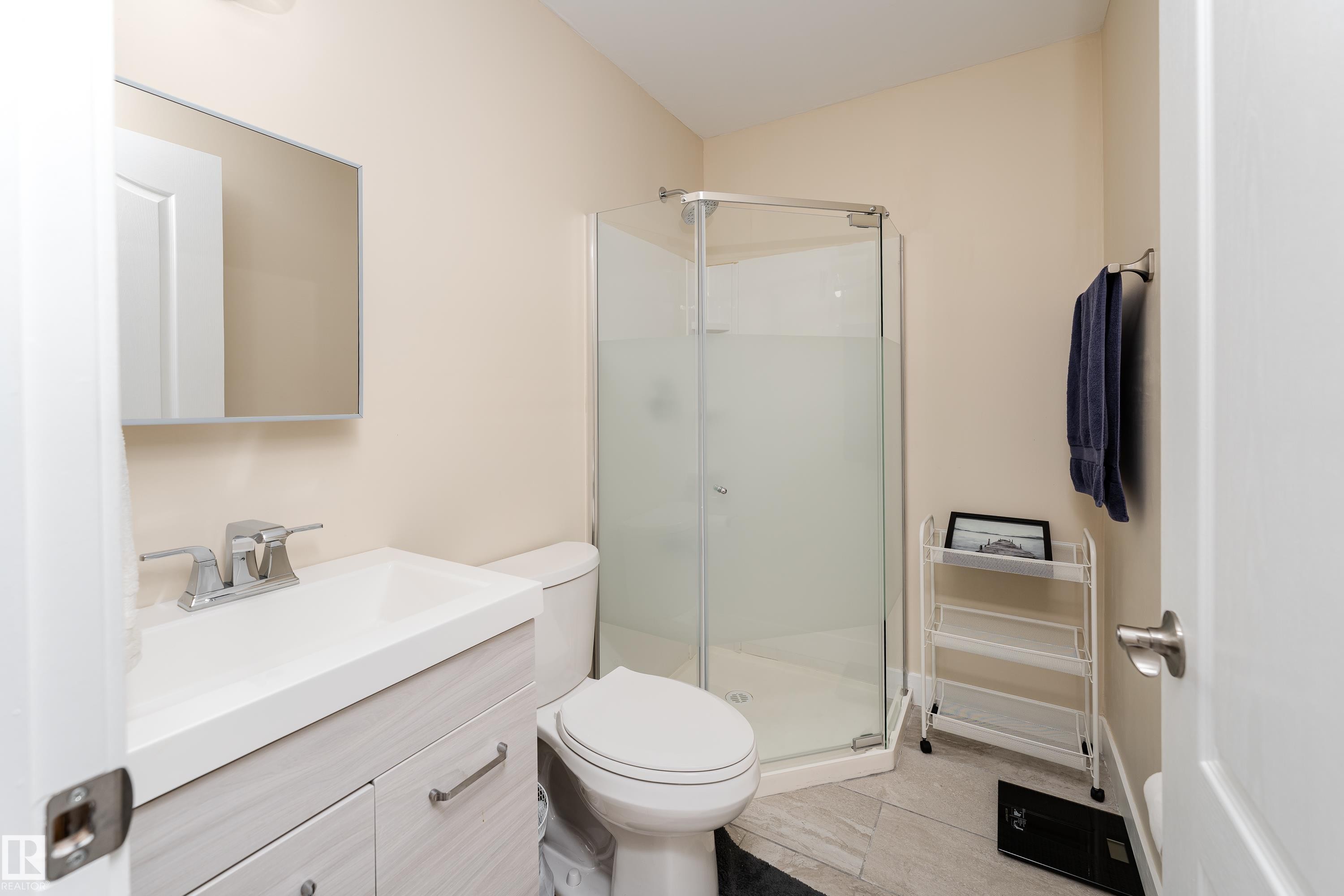 Bathroom featuring a corner shower enclosure, light wood-finish vanity with an integrated sink, polished chrome faucet, and a wall-mounted mirror - 191 Reed Place, Leduc, AB - Indoor Photo Showing Bathroom