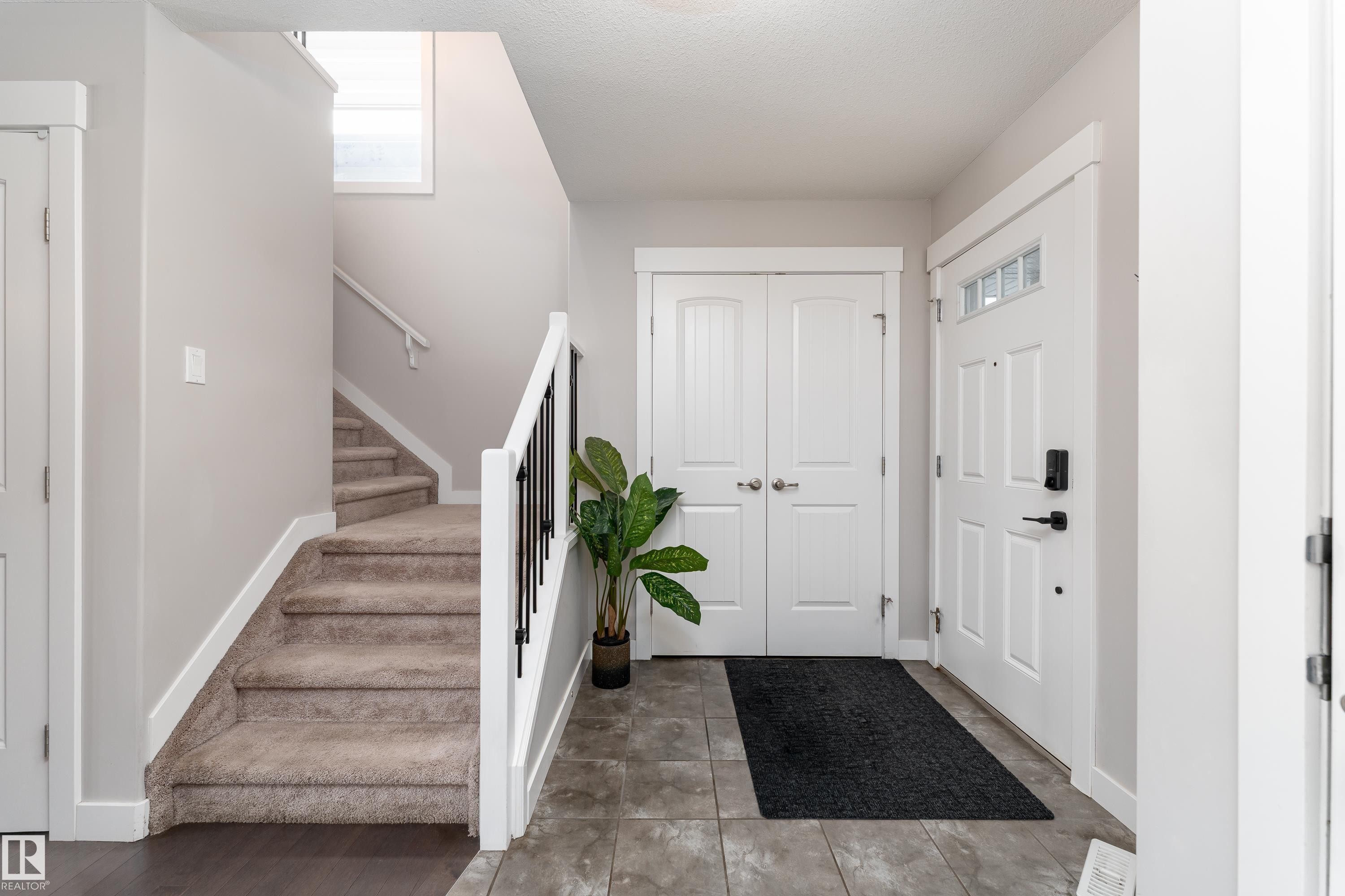 Foyer featuring a paneled front door with decorative glass inserts, durable tile flooring, and a carpeted staircase with a white railing and black spindles - 191 Reed Place, Leduc, AB - Indoor Photo Showing Other Room