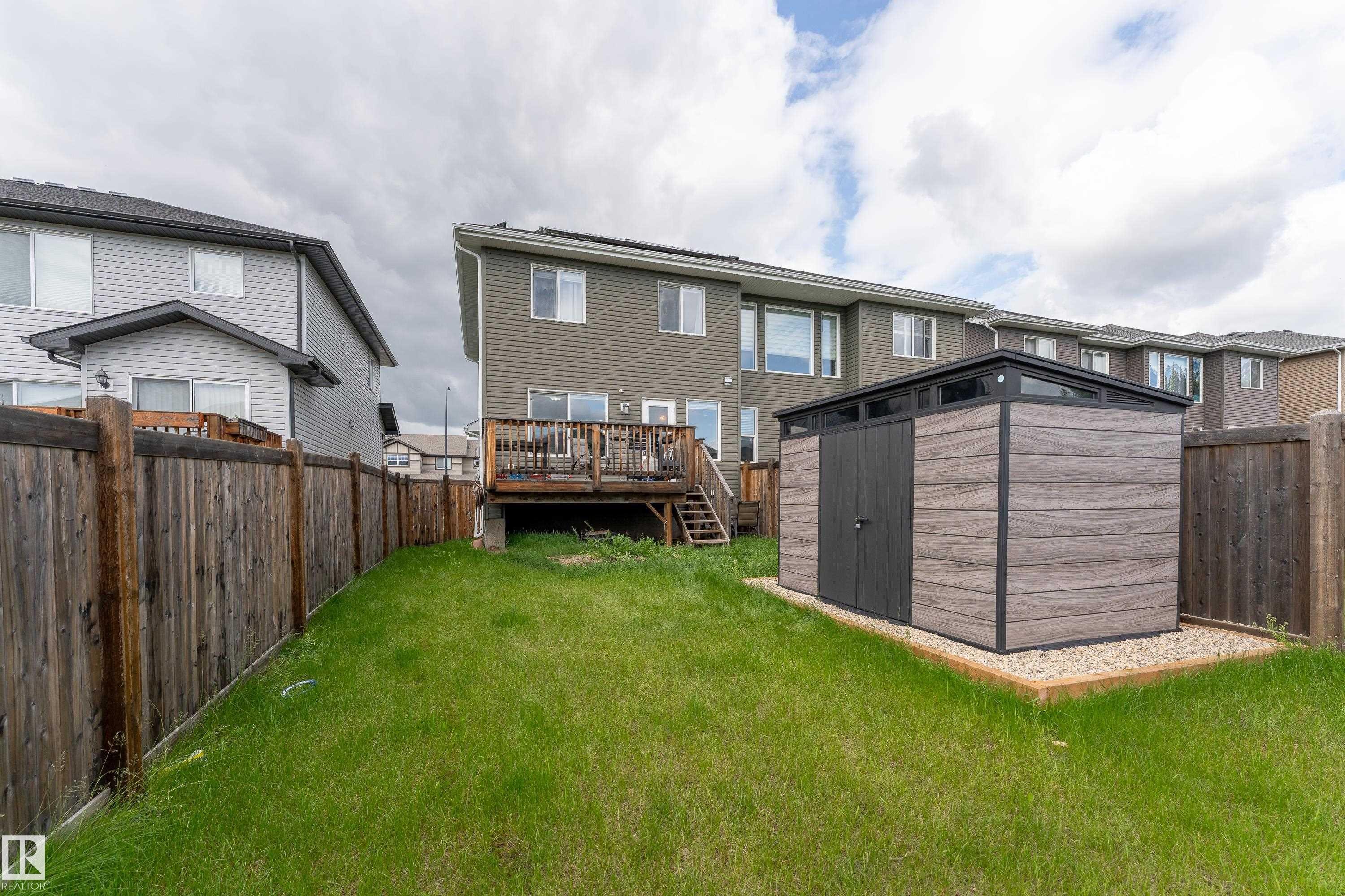 Backyard featuring a modern storage shed with wood-finish paneling and dark trim, positioned on a gravel base - 191 Reed Place, Leduc, AB - Outdoor With Exterior
