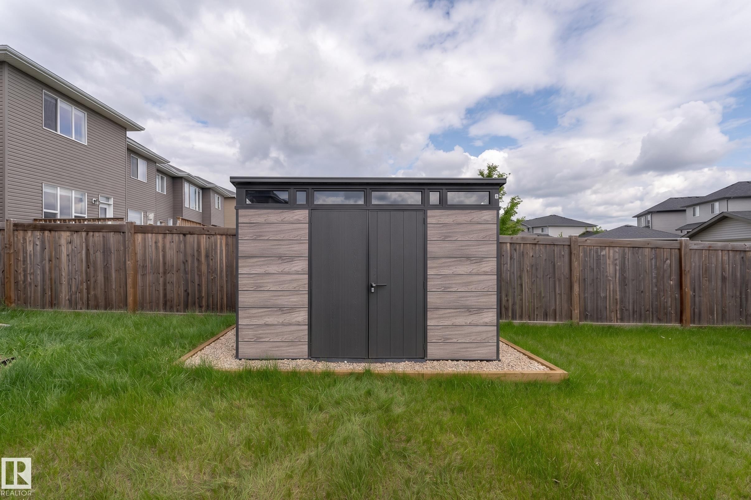 Modern storage shed featuring dual dark-toned doors, upper transom windows, and wood-grain panel siding - 191 Reed Place, Leduc, AB - Outdoor