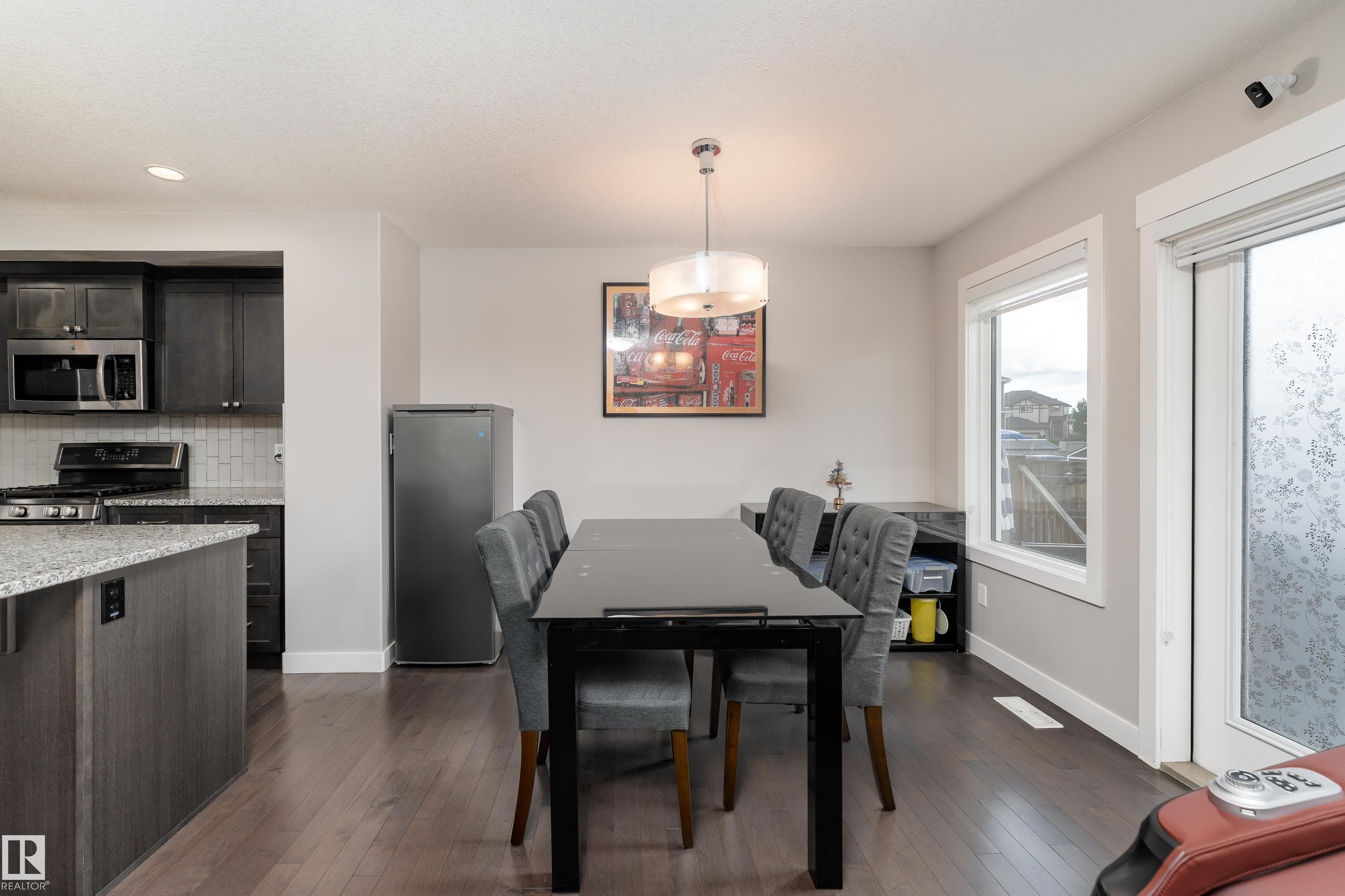 Open-concept dining area featuring dark wood-finish flooring, a contemporary chandelier, and a large window - 191 Reed Place, Leduc, AB - Indoor
