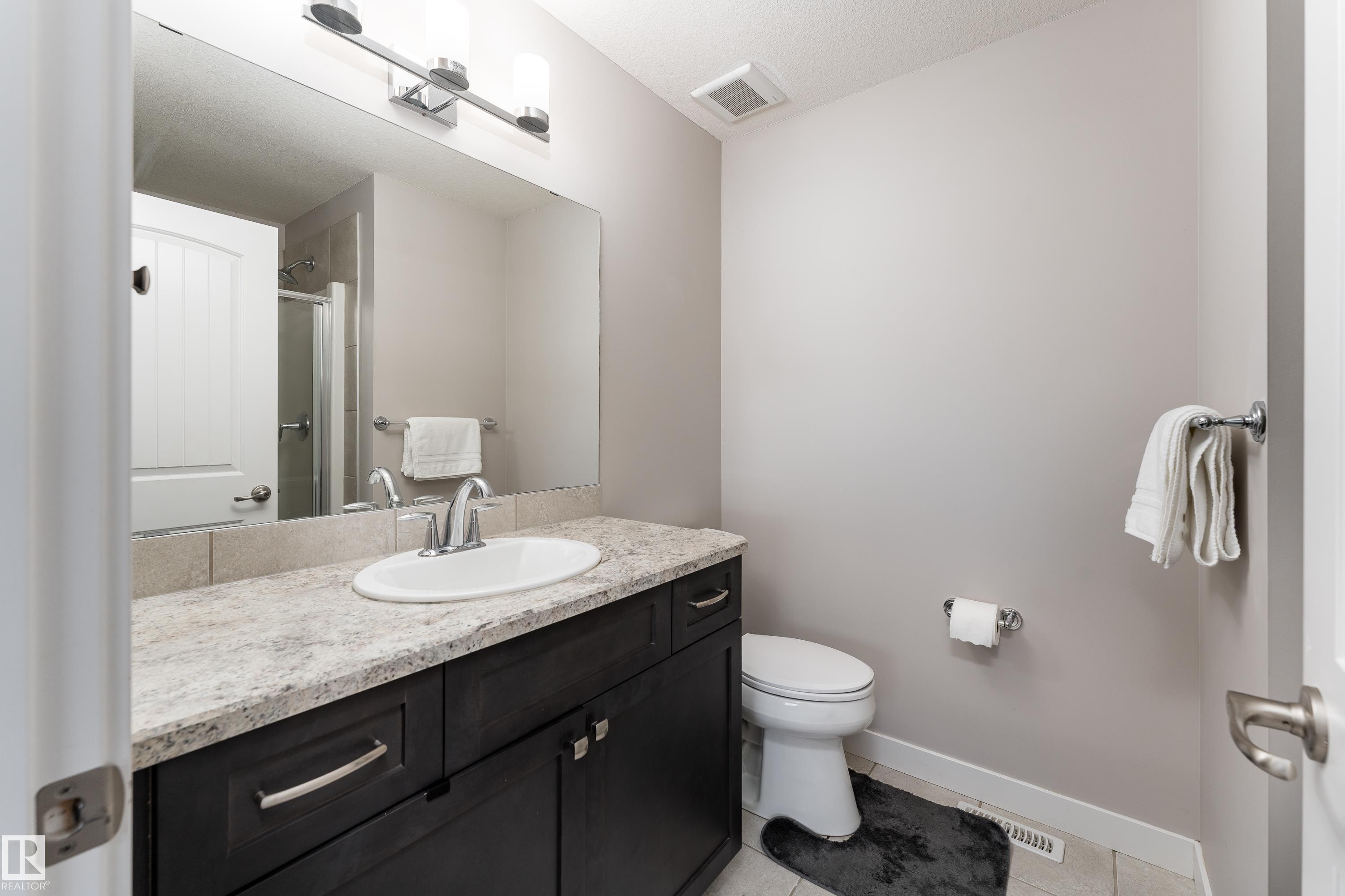 Bathroom featuring a dark wood-finish vanity with a light-colored countertop and an oval undermount sink, complemented by a chrome-finish faucet - 191 Reed Place, Leduc, AB - Indoor Photo Showing Bathroom