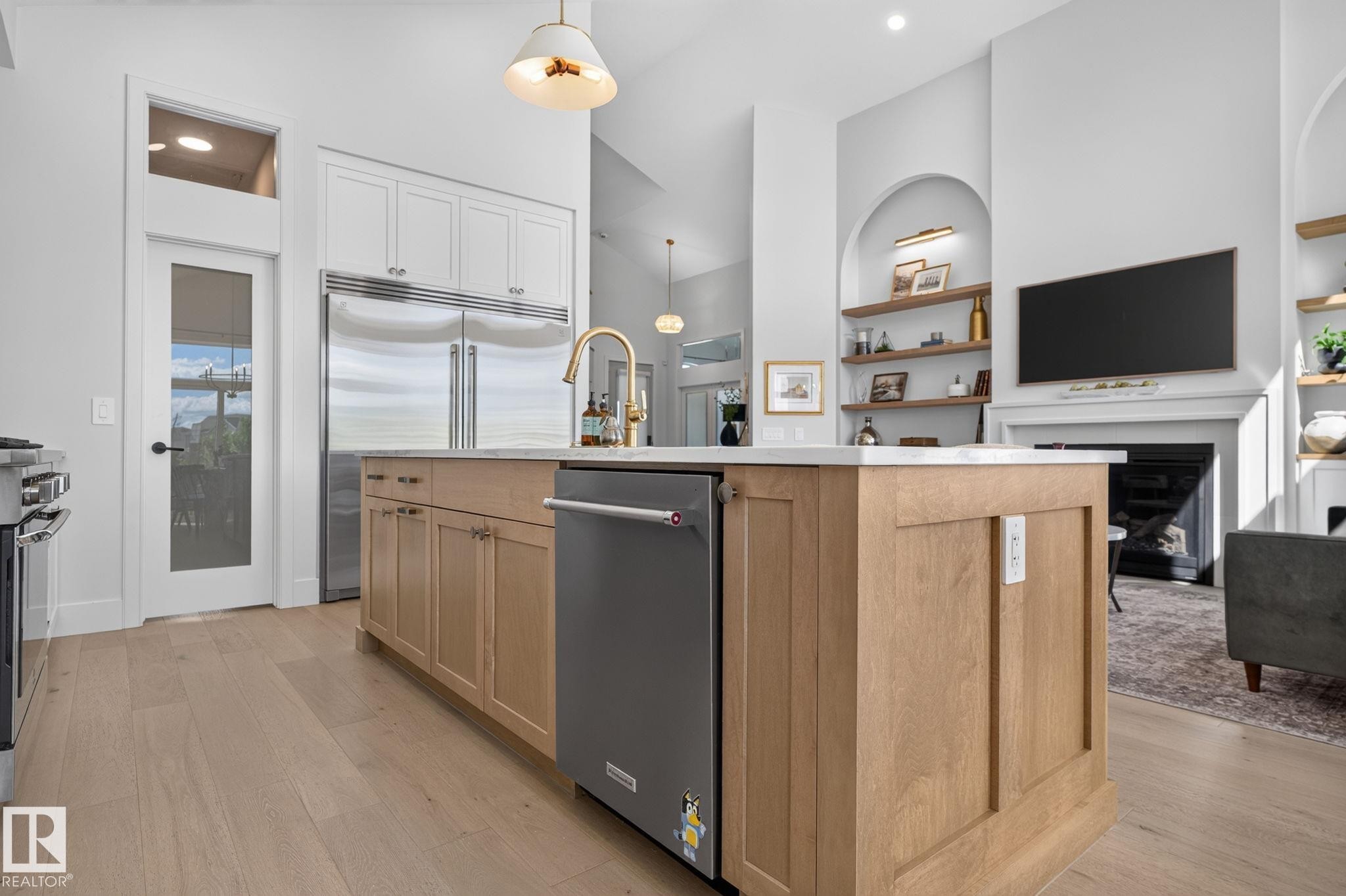 Gourmet kitchen featuring a large island with light wood cabinetry and a light-toned countertop, stainless steel appliances, and wood-finish flooring - 14 Jane Point(E), St. Albert, AB