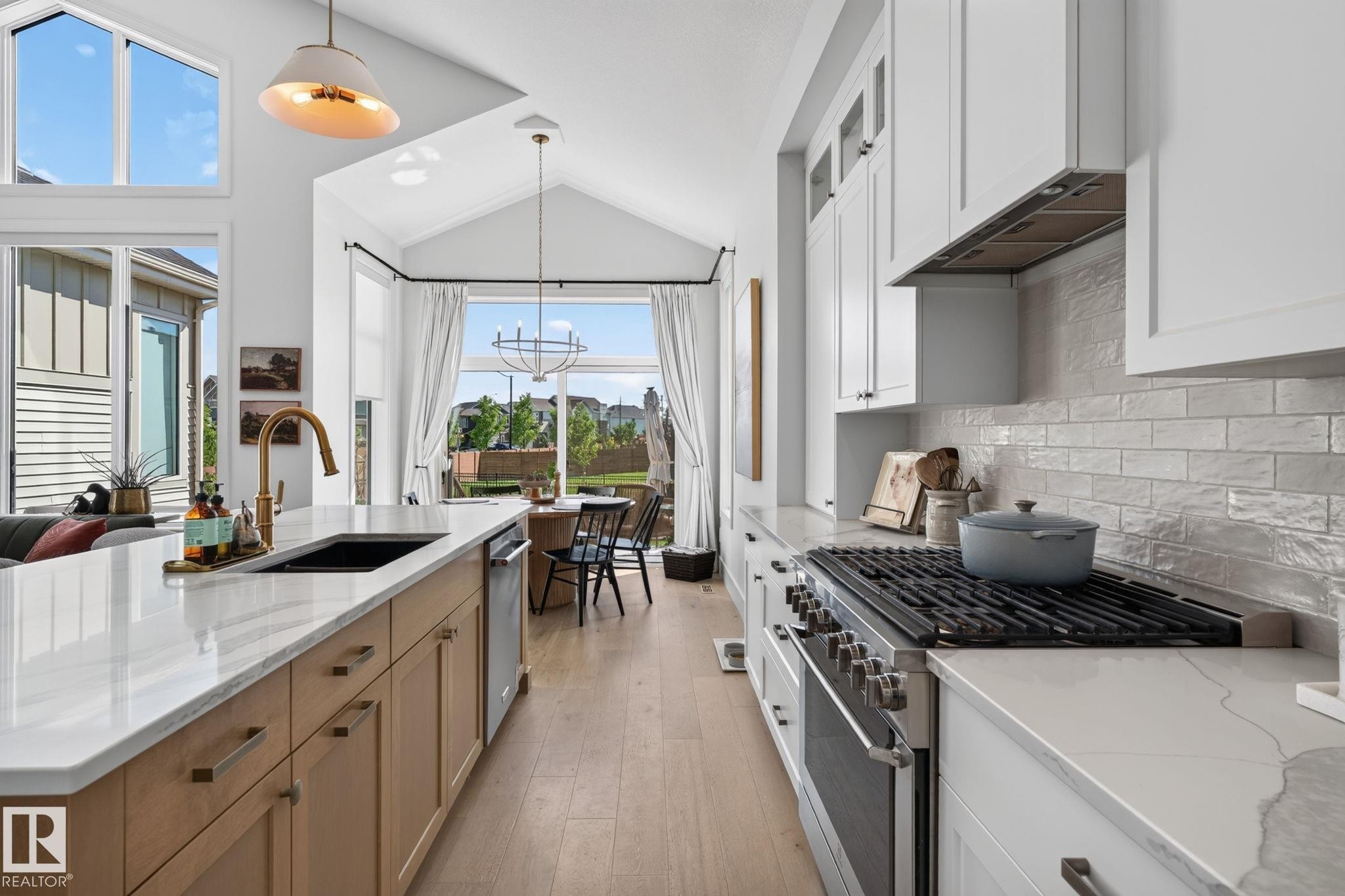 Modern kitchen featuring an expansive island with a built-in sink and gold-tone faucet, light wood-finish cabinetry, and white countertops - 14 Jane Point(E), St. Albert, AB