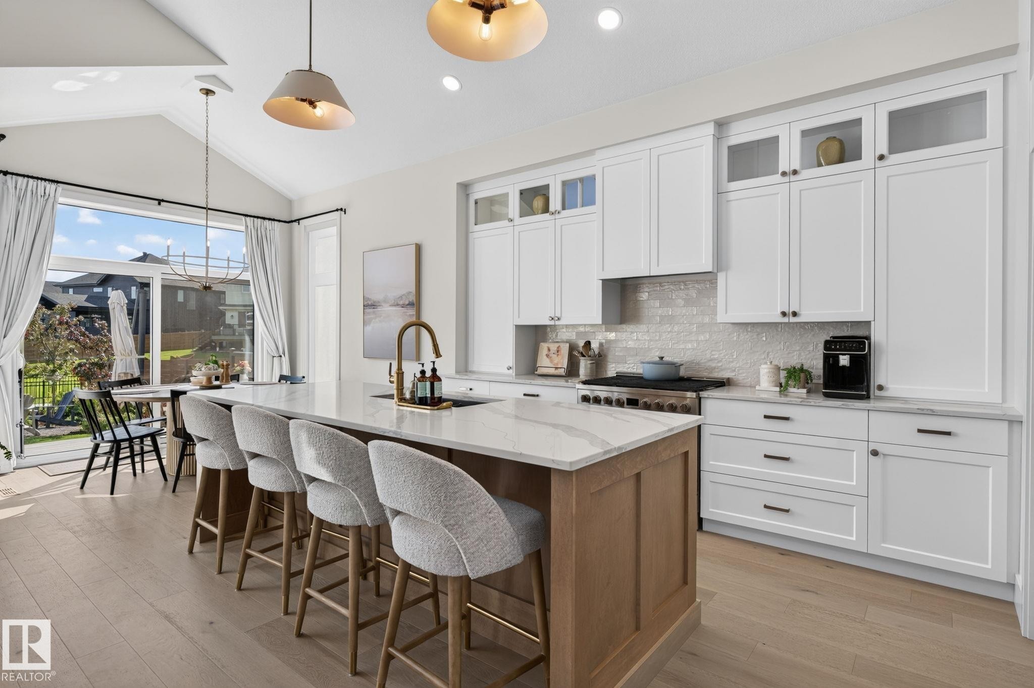 Gourmet kitchen with a large central island, light wood-finish flooring, white shaker-style cabinetry with upper glass-front accents, a light-toned tile backsplash, and stainless steel appliances - 14 Jane Point(E), St. Albert, AB