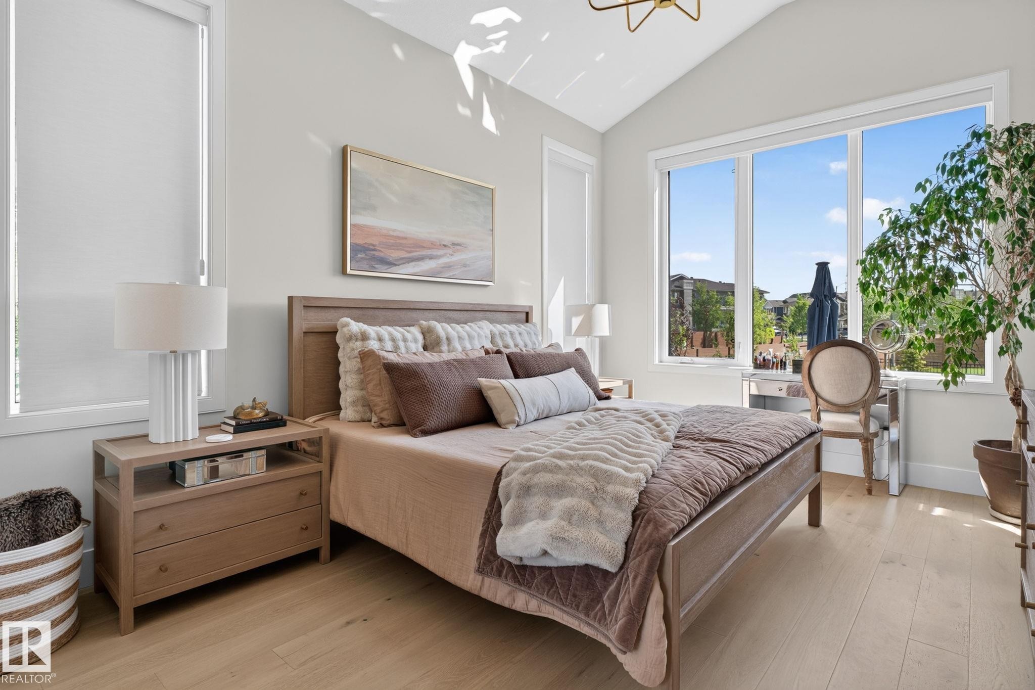 Vaulted ceiling bedroom featuring light wood-finish flooring, a contemporary chandelier, large picture windows, and roller shades - 14 Jane Point(E), St. Albert, AB