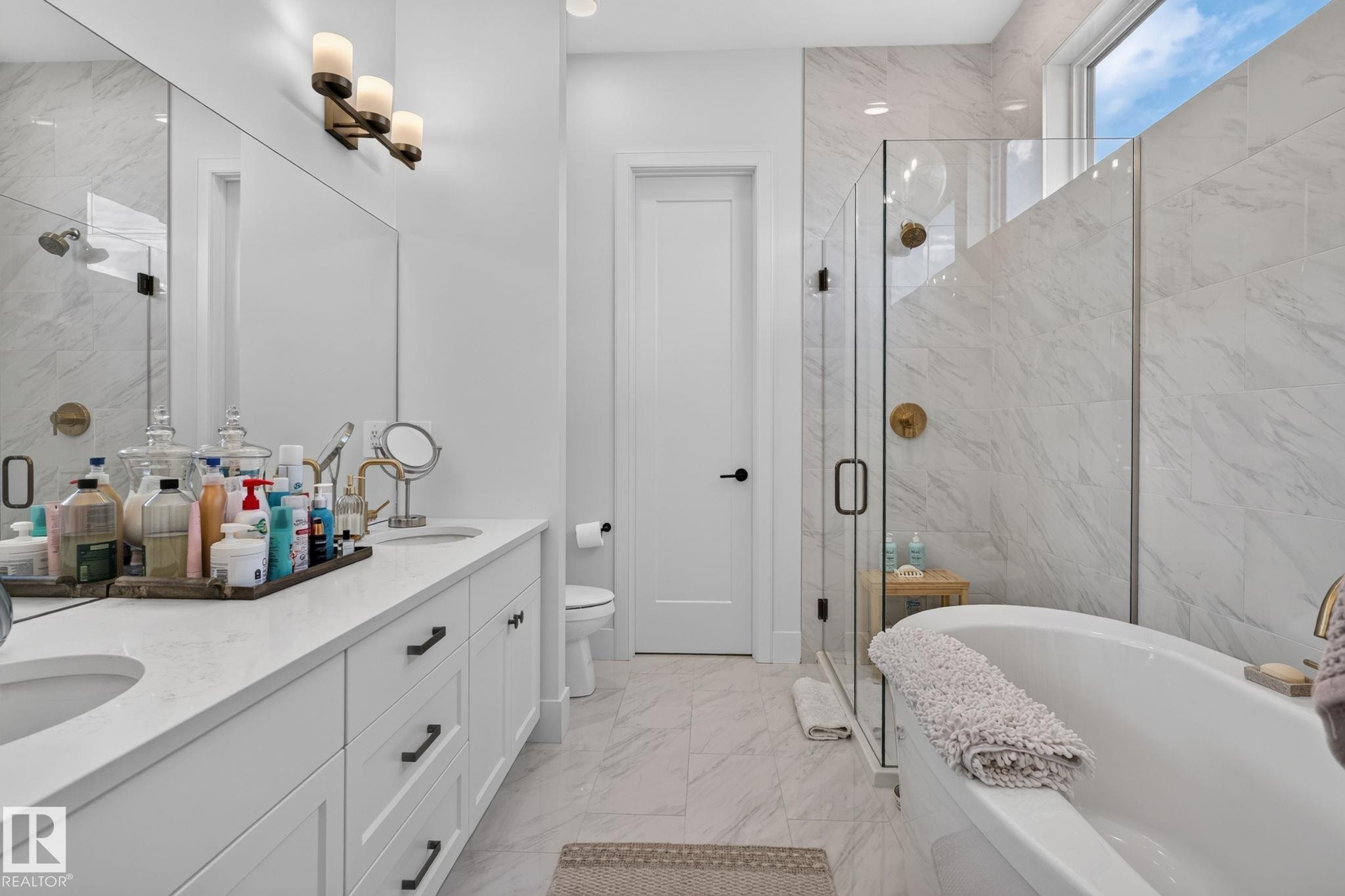 Spacious bathroom featuring a freestanding soaking tub, a frameless glass shower enclosure, a dual vanity with undermount sinks, and a large privacy window - 14 Jane Point(E), St. Albert, AB