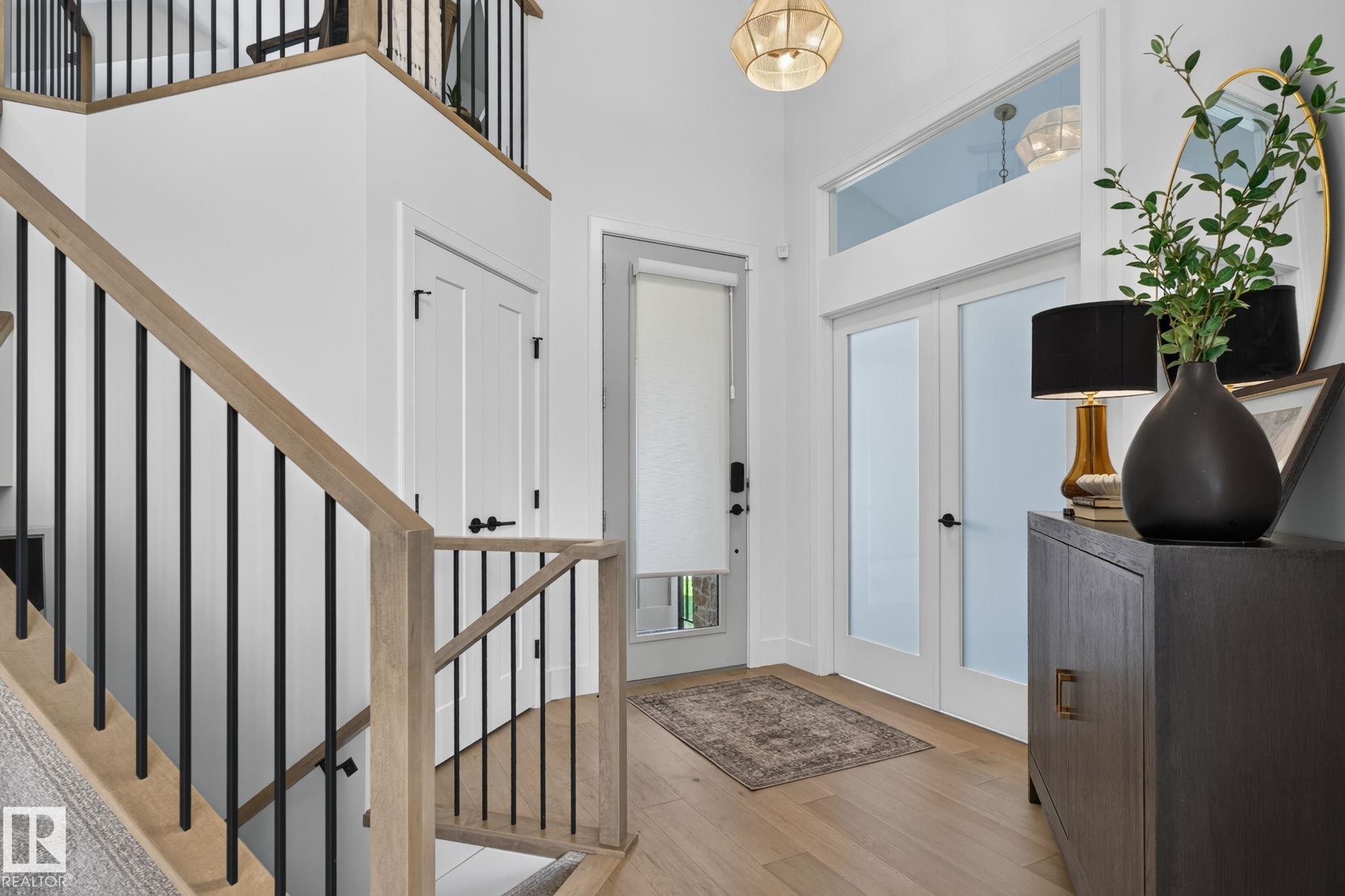 Foyer entryway featuring light wood-finish flooring, a contemporary chandelier, a white paneled door, and double doors with frosted glass panels - 14 Jane Point(E), St. Albert, AB