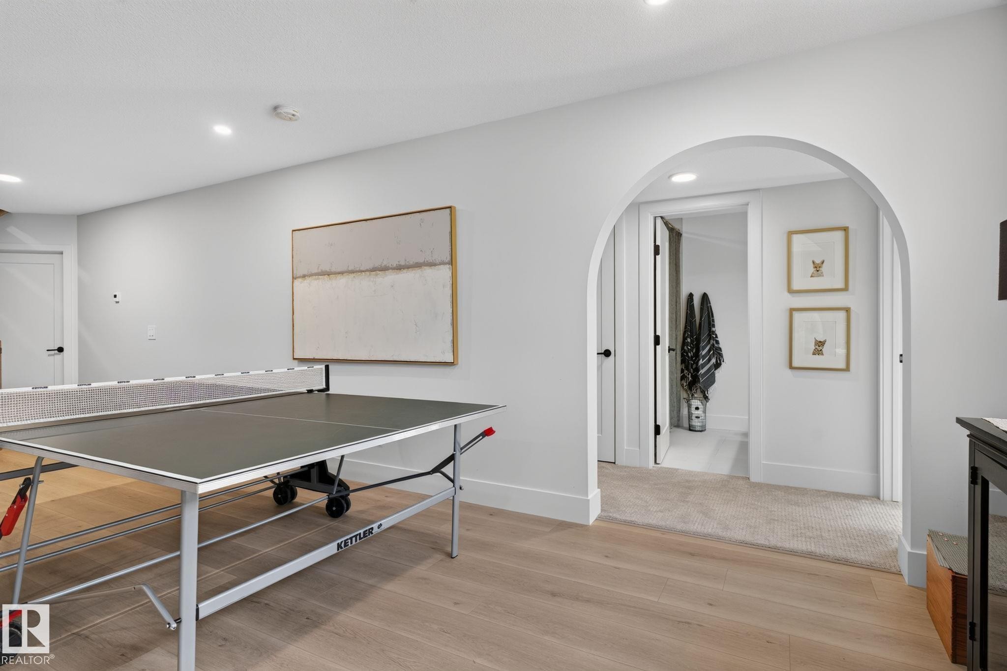 Spacious room featuring light wood-finish flooring, recessed lighting, and an arched doorway leading to a carpeted hall - 14 Jane Point(E), St. Albert, AB