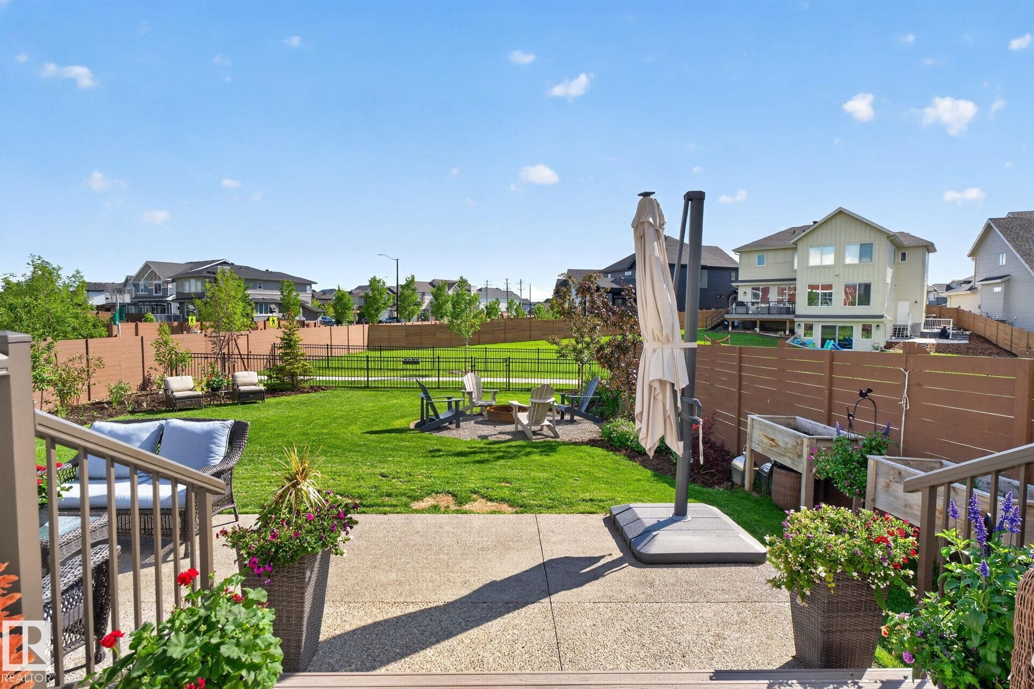Expansive backyard featuring a concrete patio, a manicured lawn, a fire pit area, a brown privacy fence, and mature trees - 14 Jane Point(E), St. Albert, AB