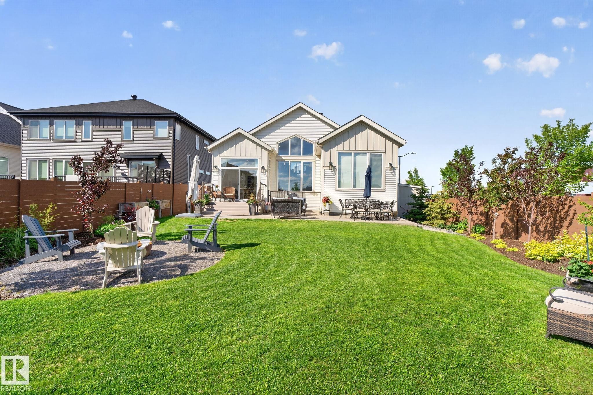 Expansive backyard featuring a manicured lawn, a gravel patio with a fire pit, and mature landscaping - 14 Jane Point(E), St. Albert, AB