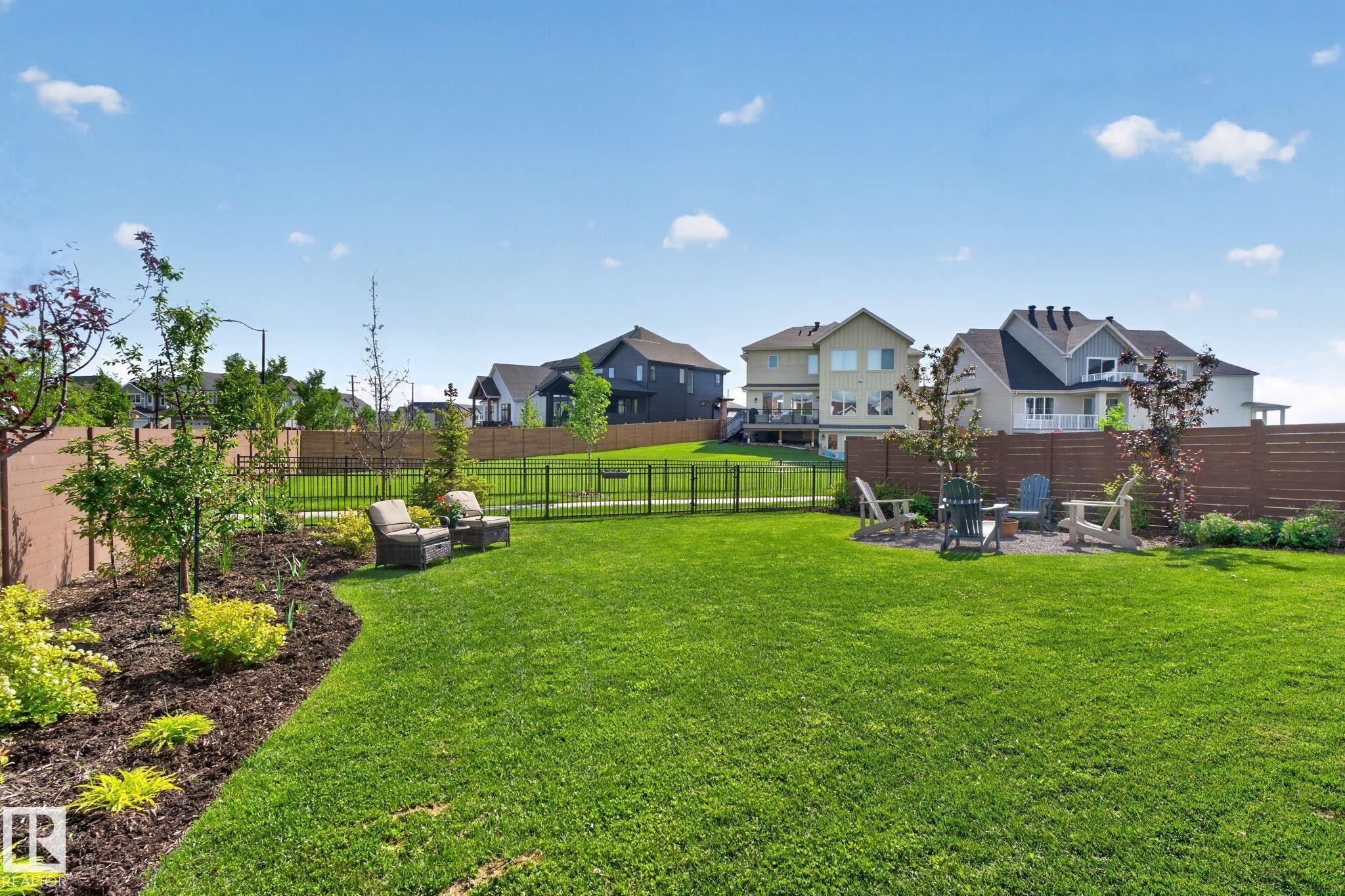 Expansive backyard featuring a lush lawn, a dedicated fire pit area, and landscaped garden beds with mature plantings - 14 Jane Point(E), St. Albert, AB