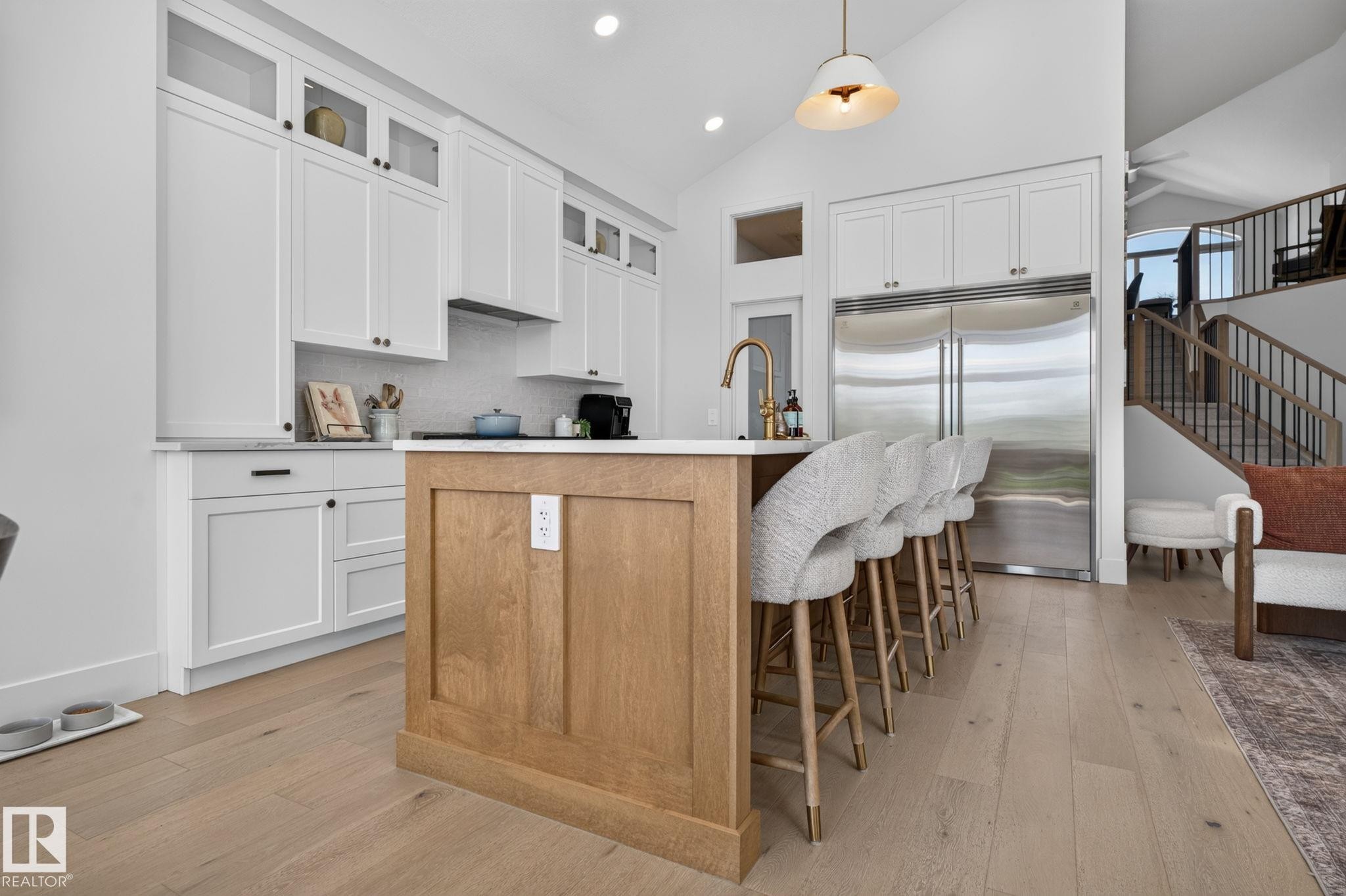 Contemporary kitchen featuring a light wood-finish island with seating, white shaker cabinetry, stainless steel appliances, and a vaulted ceiling - 14 Jane Point(E), St. Albert, AB