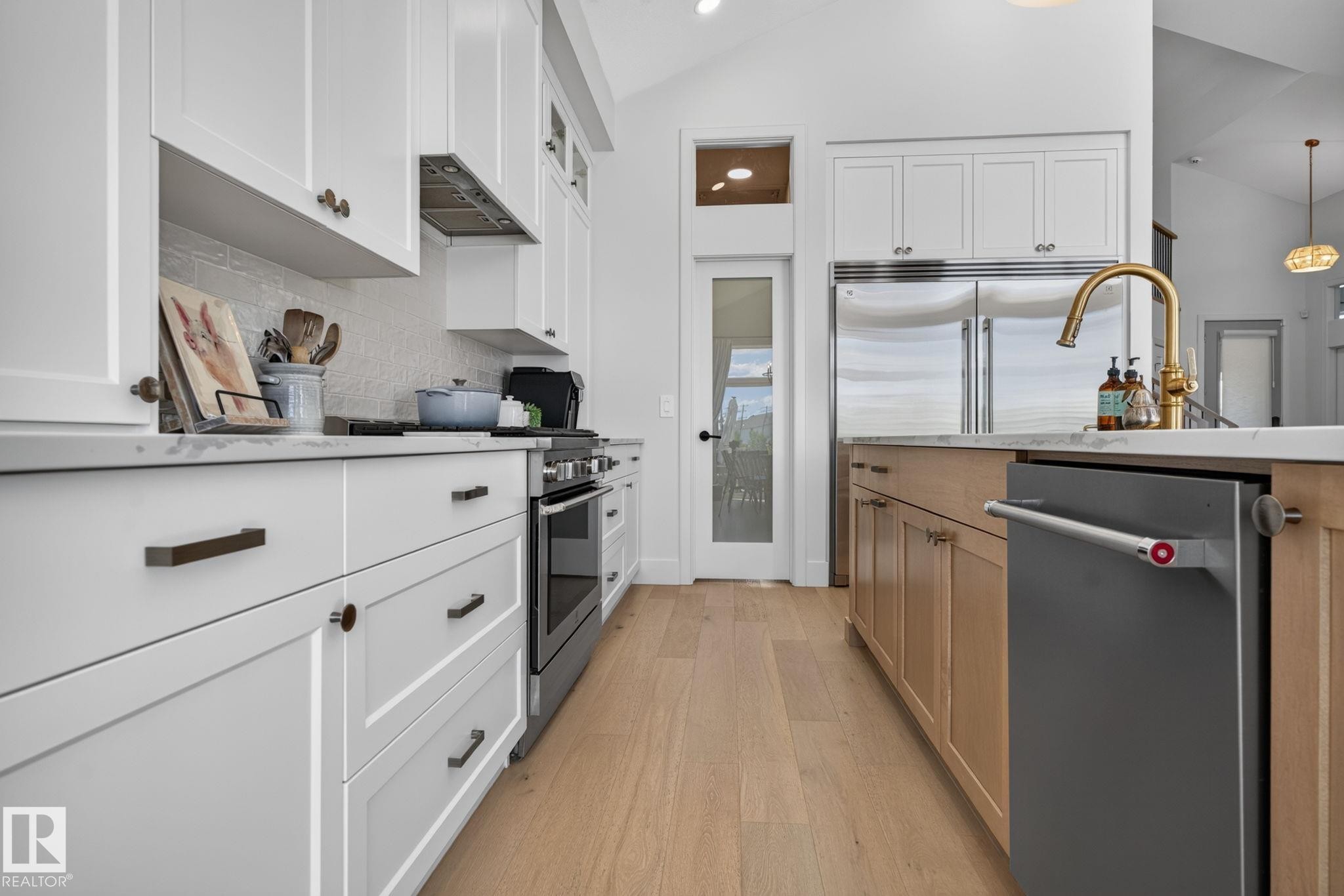 Bright kitchen featuring white shaker cabinetry, stainless steel appliances, a brass-finish faucet, light wood-finish flooring, and a glass-paneled pantry door - 14 Jane Point(E), St. Albert, AB