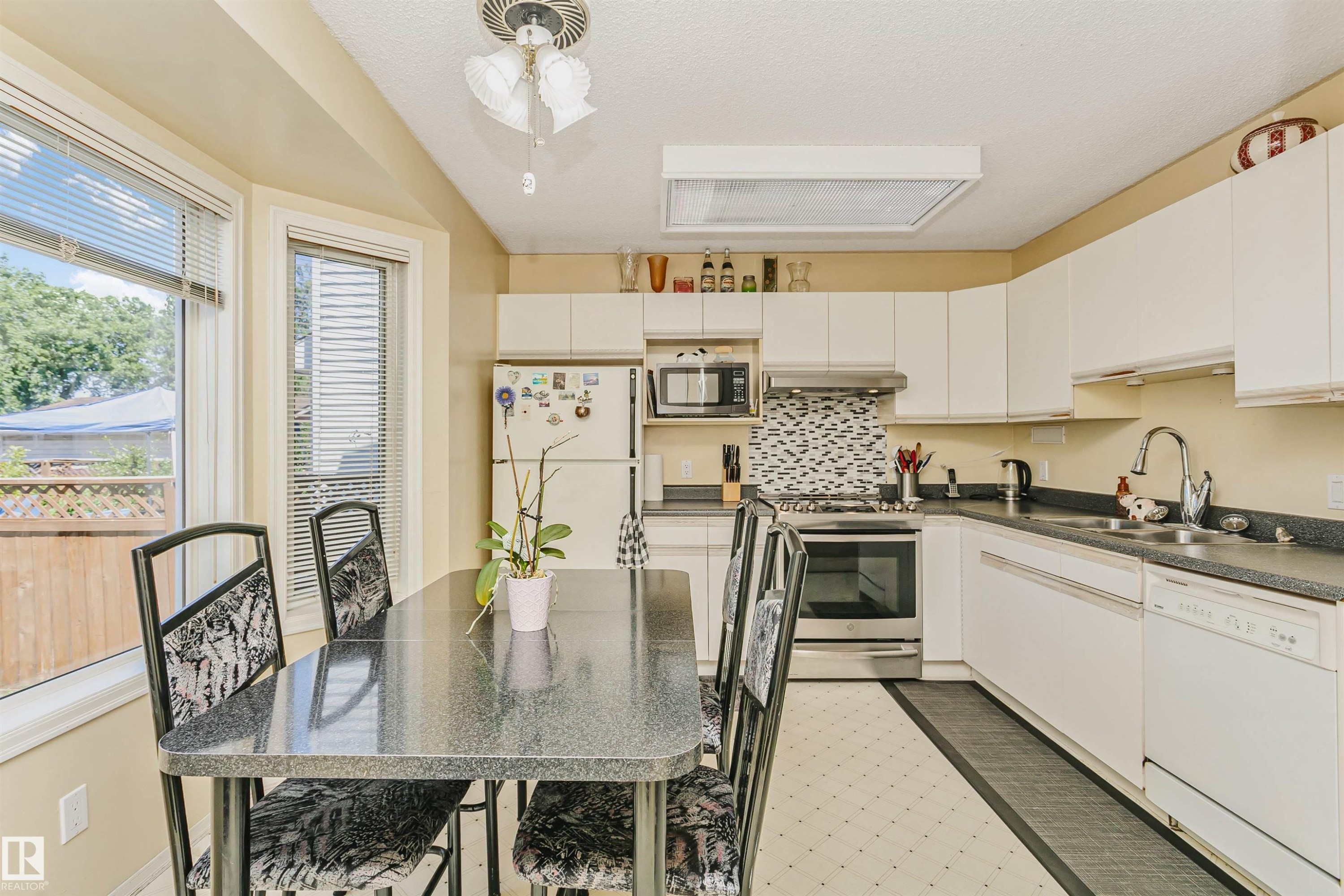 Kitchen featuring white cabinetry, dark countertops, a mosaic tile backsplash, and stainless steel appliances - 1612 80A Street, Edmonton, AB