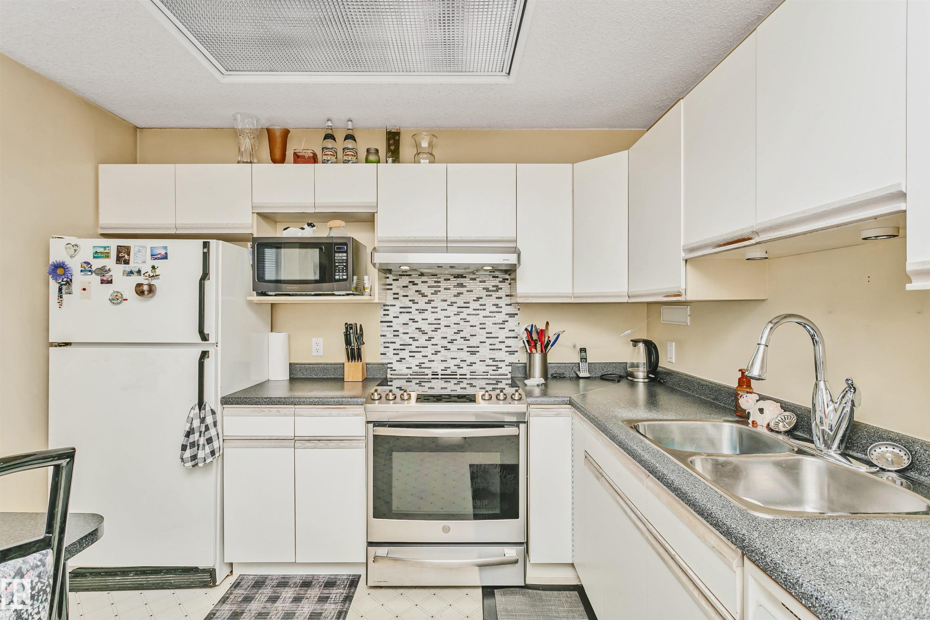 Kitchen featuring white cabinetry, gray speckled countertops, a mosaic tile backsplash, and stainless steel appliances including a range and double basin sink - 1612 80A Street, Edmonton, AB
