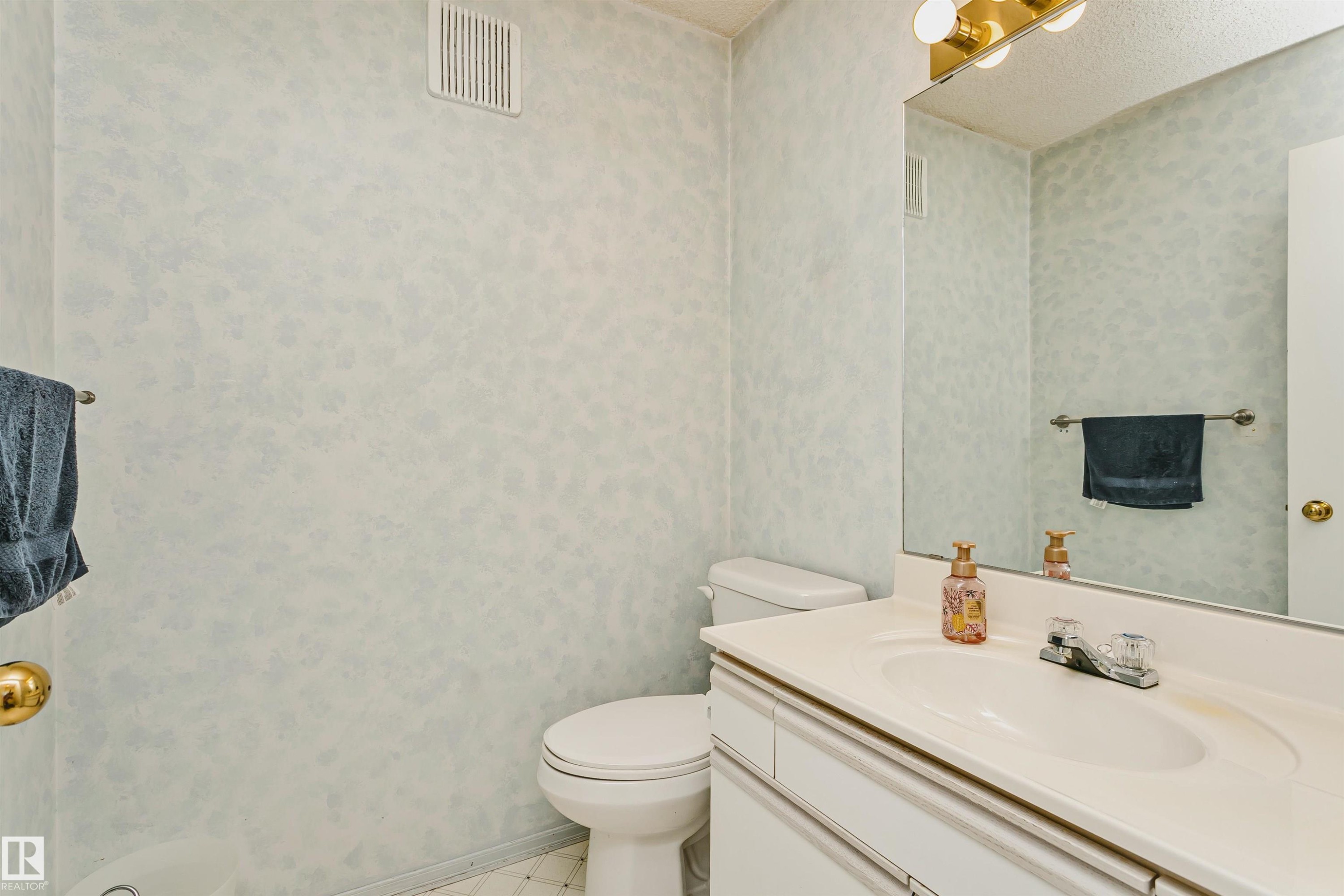 Bathroom featuring a single vanity with an integrated sink, polished chrome faucet, and a large wall-mounted mirror - 1612 80A Street, Edmonton, AB
