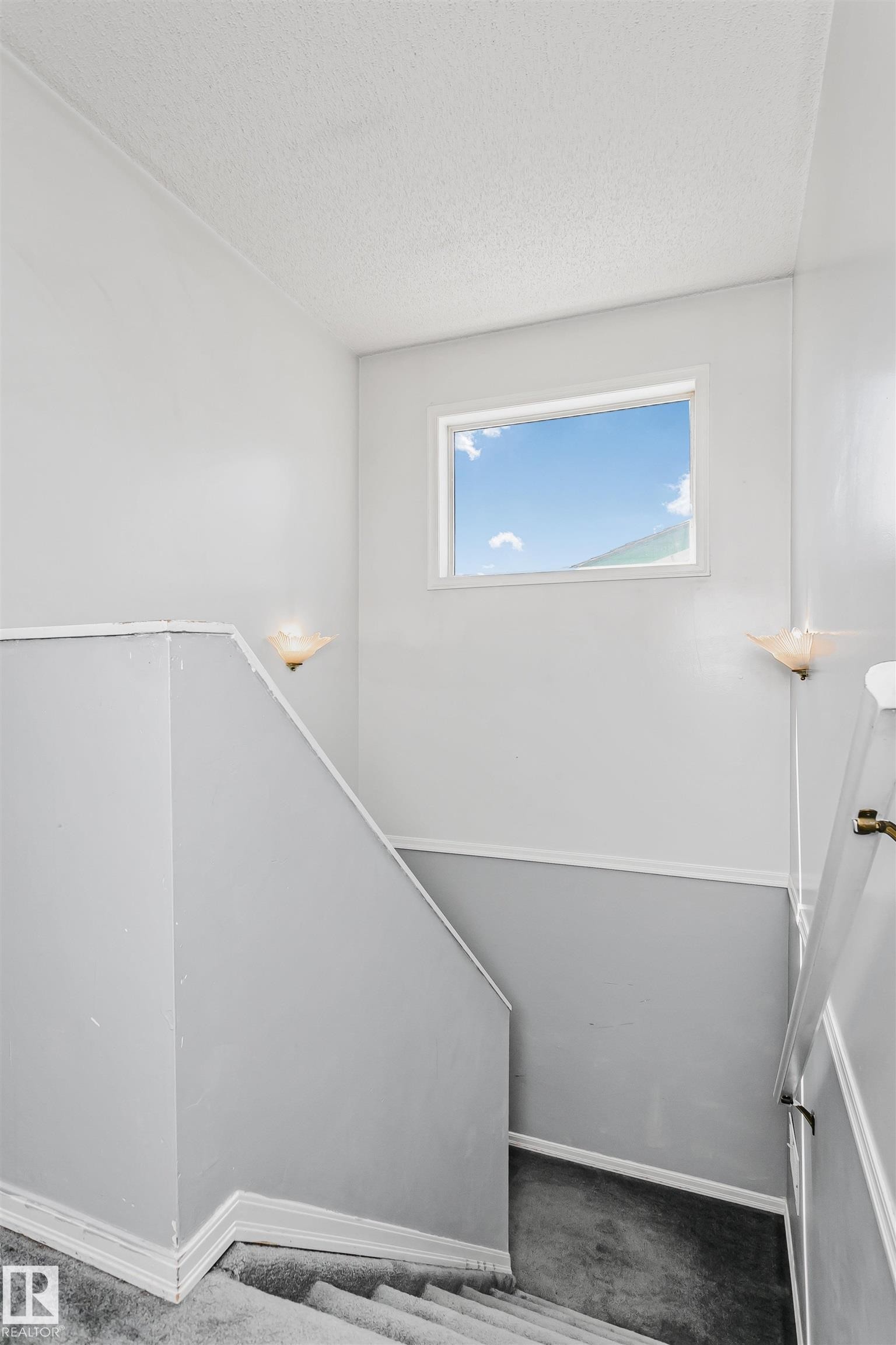 Staircase featuring a window, wall-mounted sconces, and carpeted steps - 1612 80A Street, Edmonton, AB