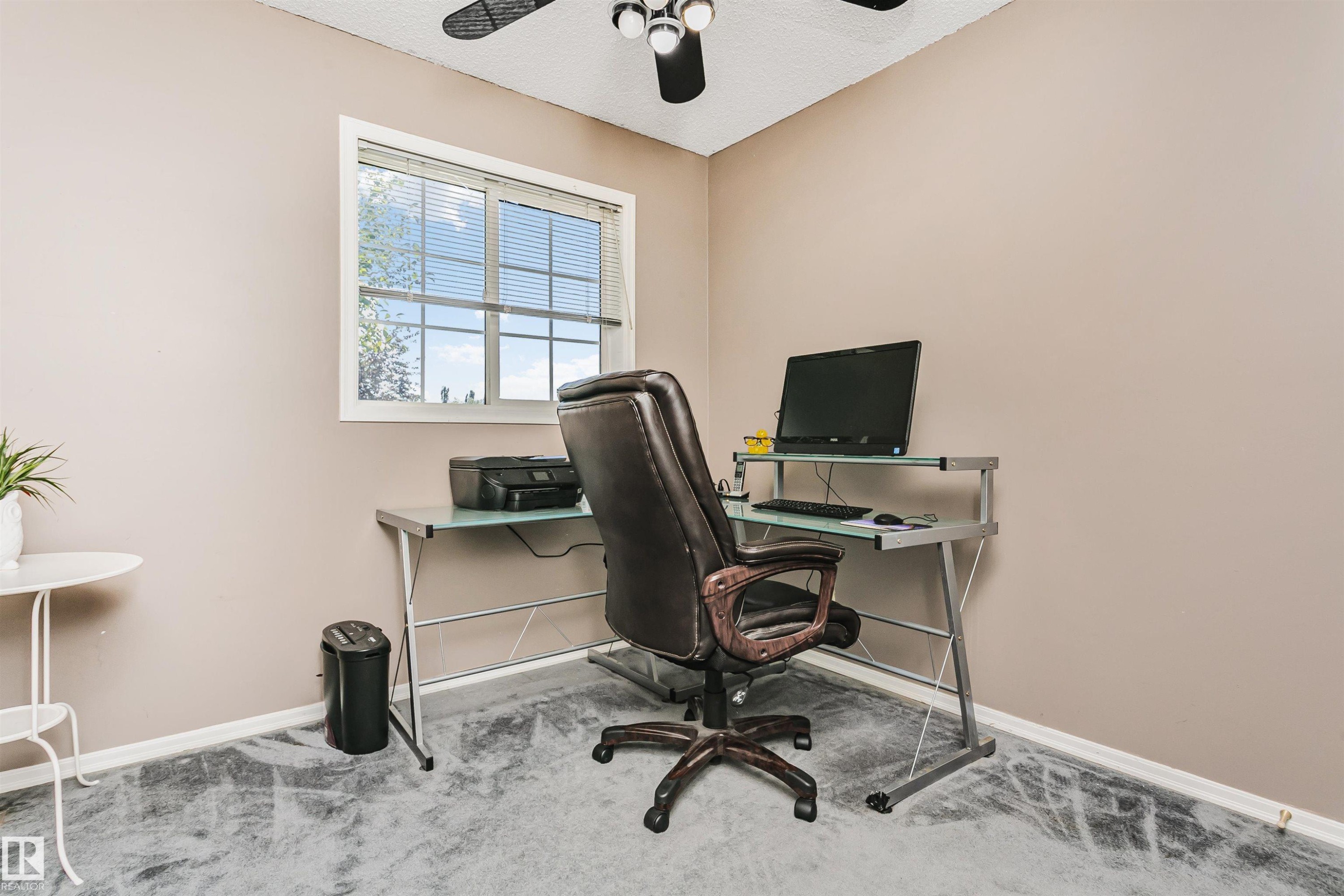 Neutral-toned room featuring a single window with blinds, light gray wall-to-wall carpeting, and a ceiling fan with black blades and integrated lighting - 1612 80A Street, Edmonton, AB