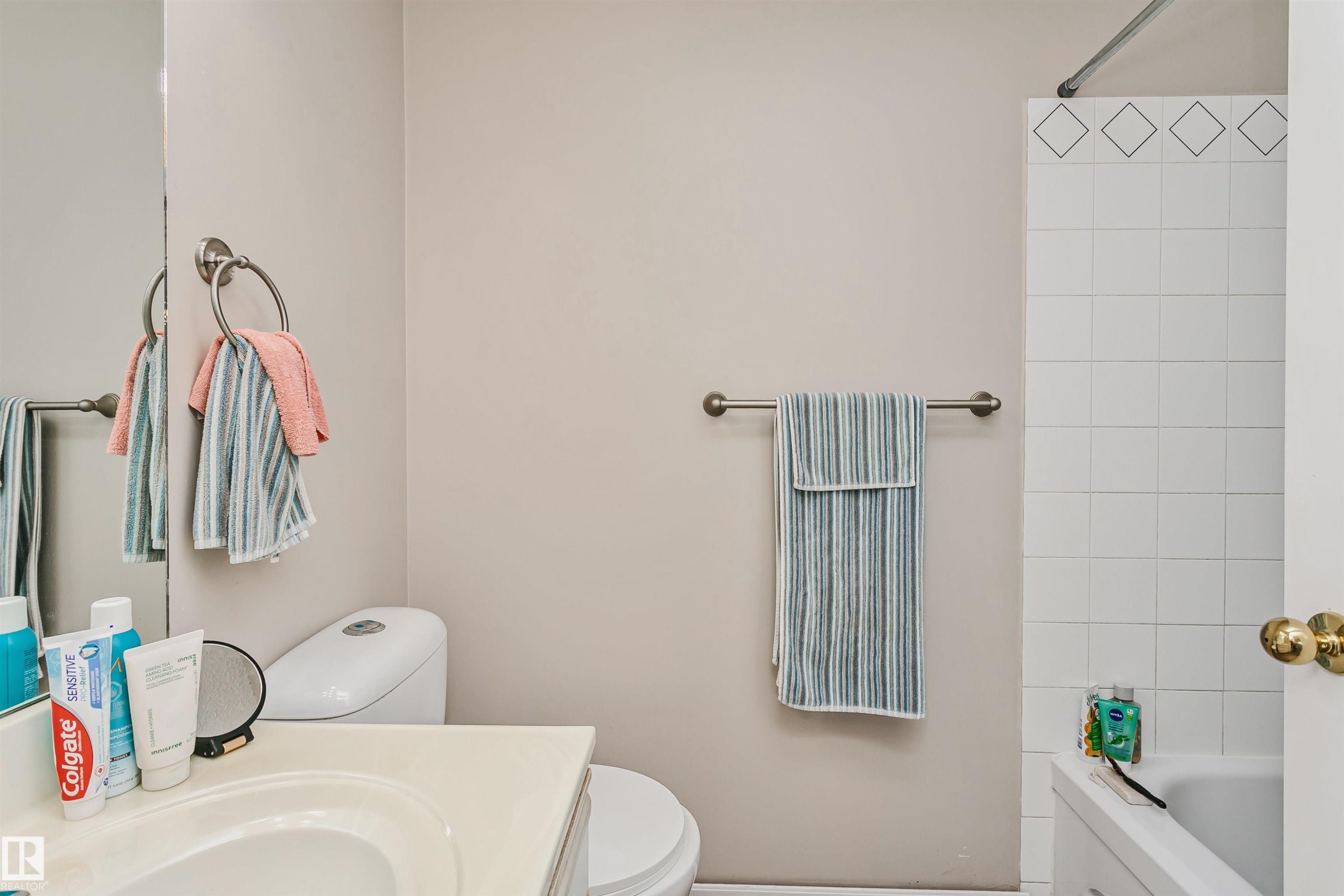 Bathroom featuring a white vanity with an integrated sink, a commode, and a shower-over-tub combination with white square tiles and a decorative border - 1612 80A Street, Edmonton, AB